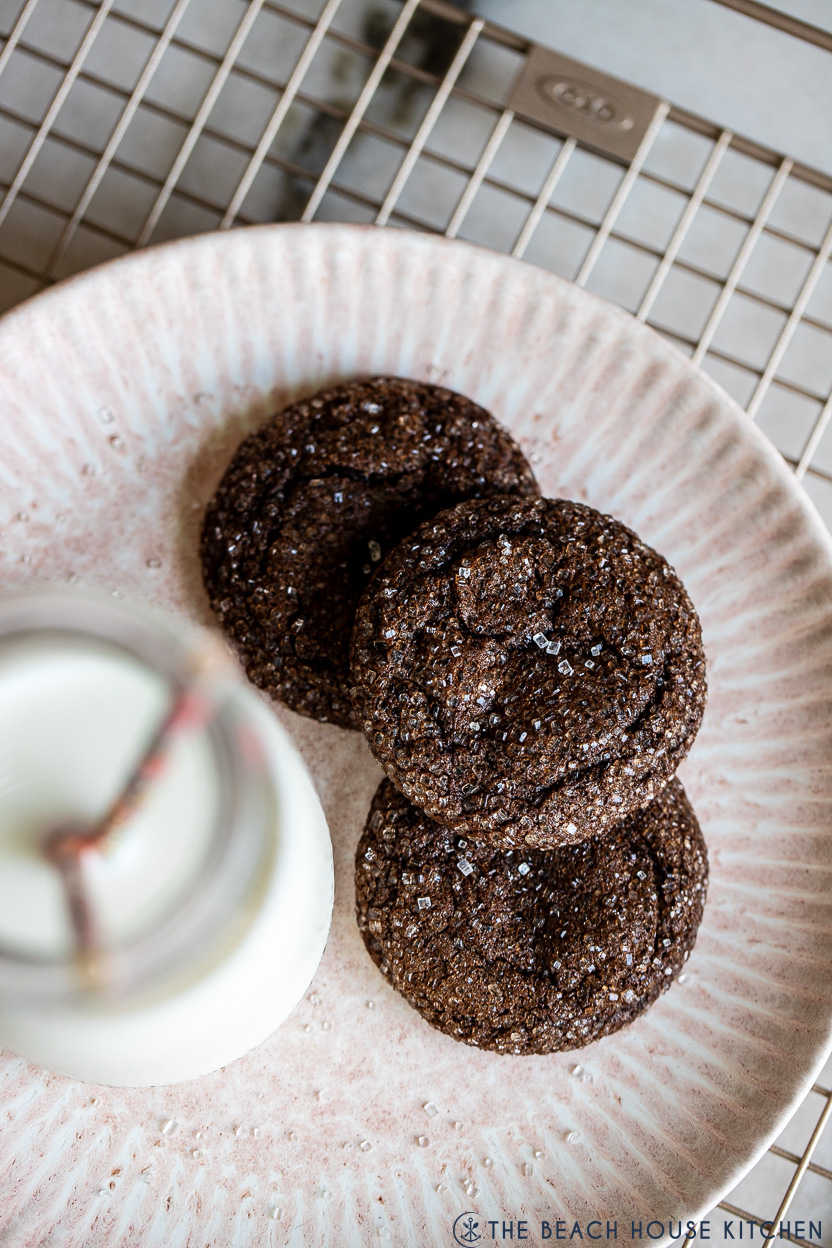 Overhead photo of a plate of three chocolate sugar cookies and a bottle of milk with two straws