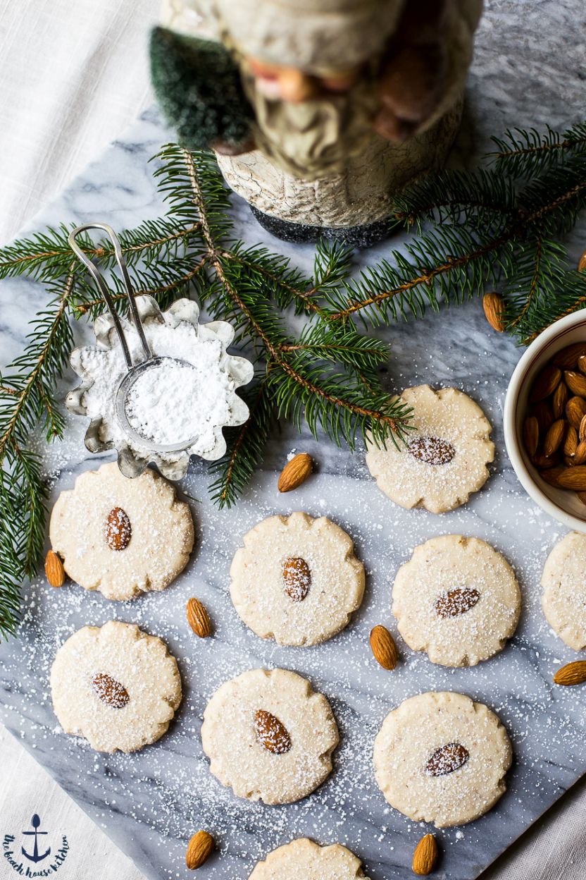 Overhead photo of a marble board topped with almond cookies, some Christmas greens and a Santa figure