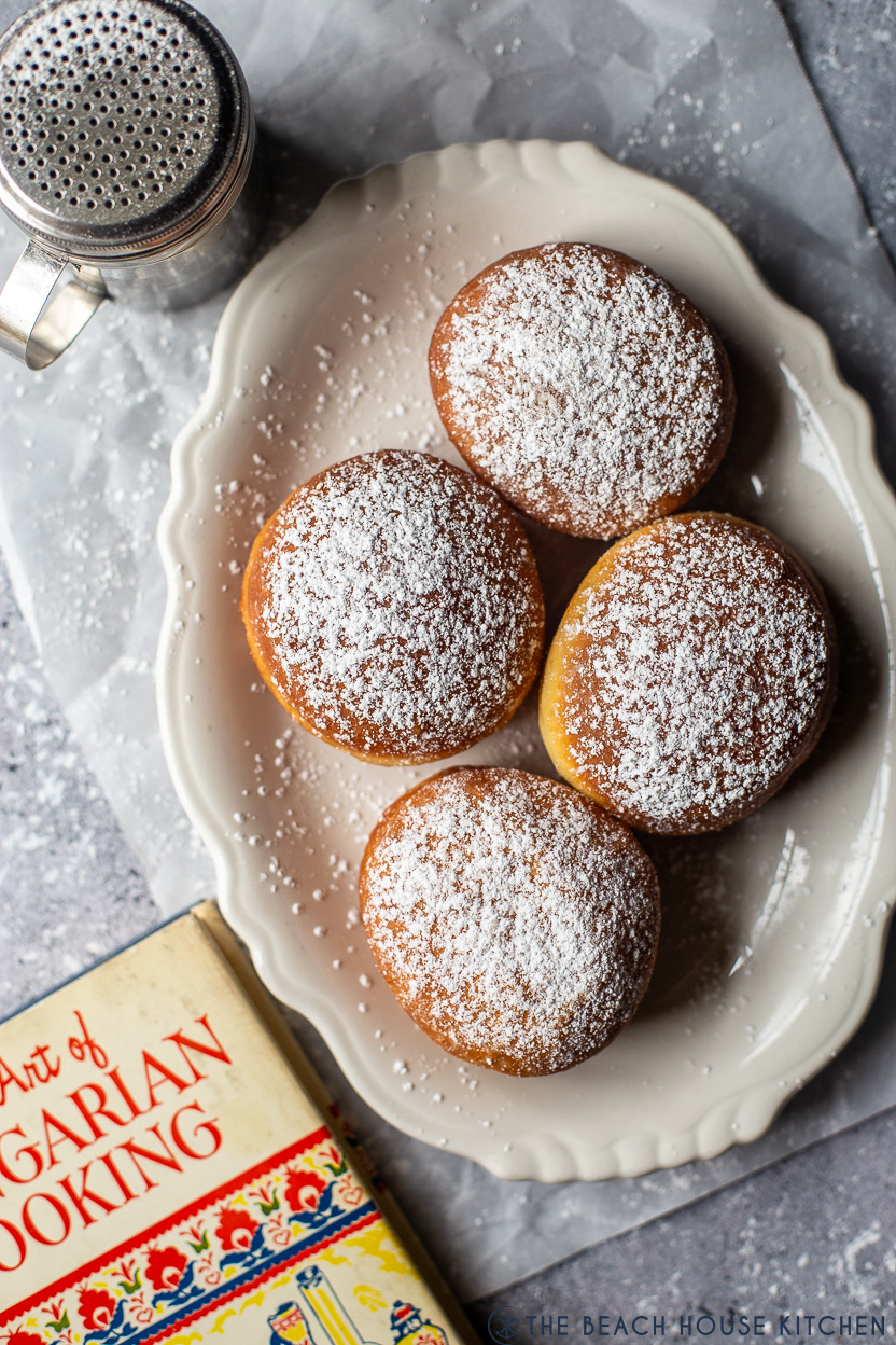 Overhead photo of an oval plate of 4 Hungarian doughnuts with a book off to the left side