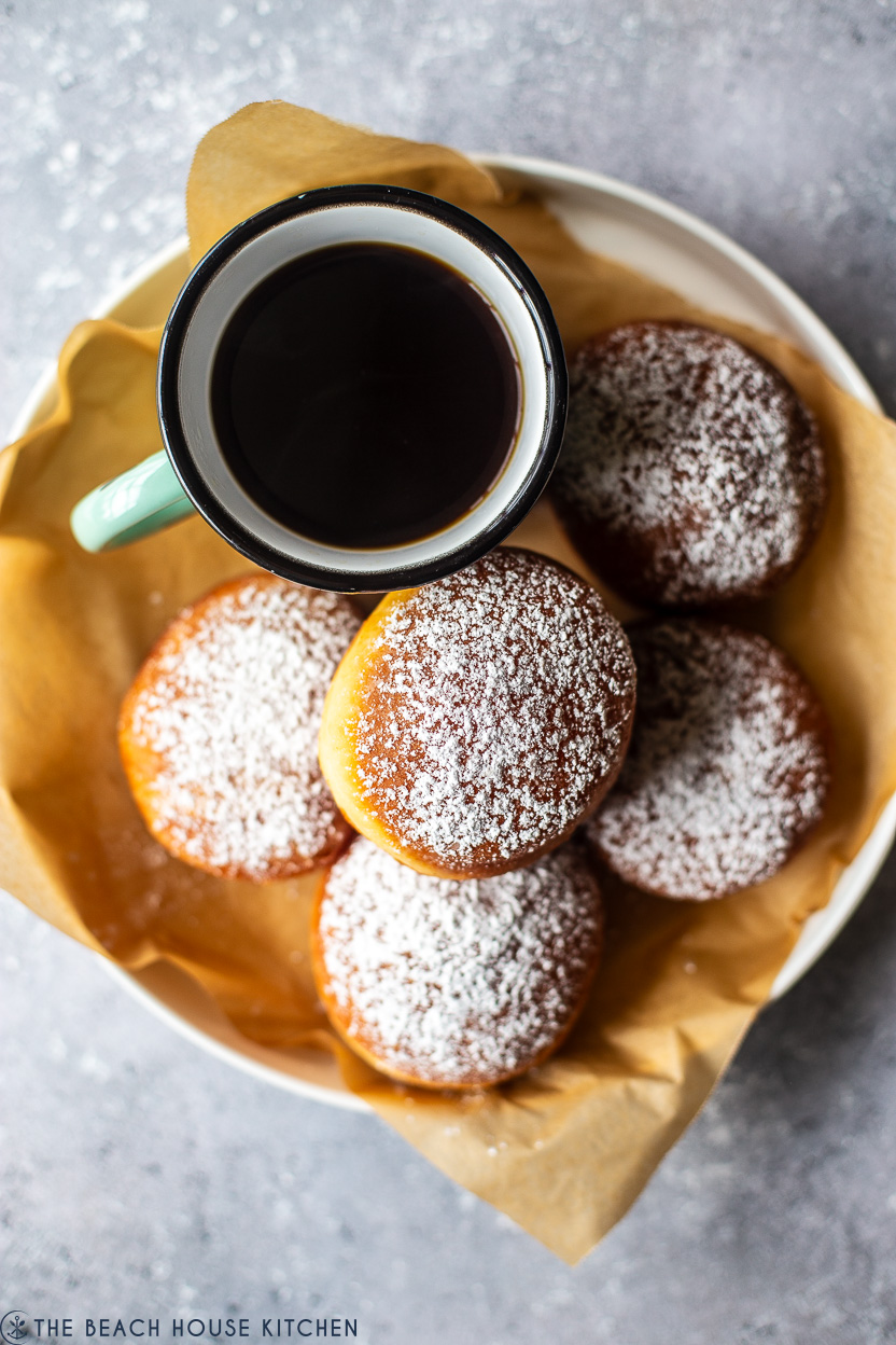 Overhead photo of a dish filled with powdered Hungarian doughnuts and a mug of coffee