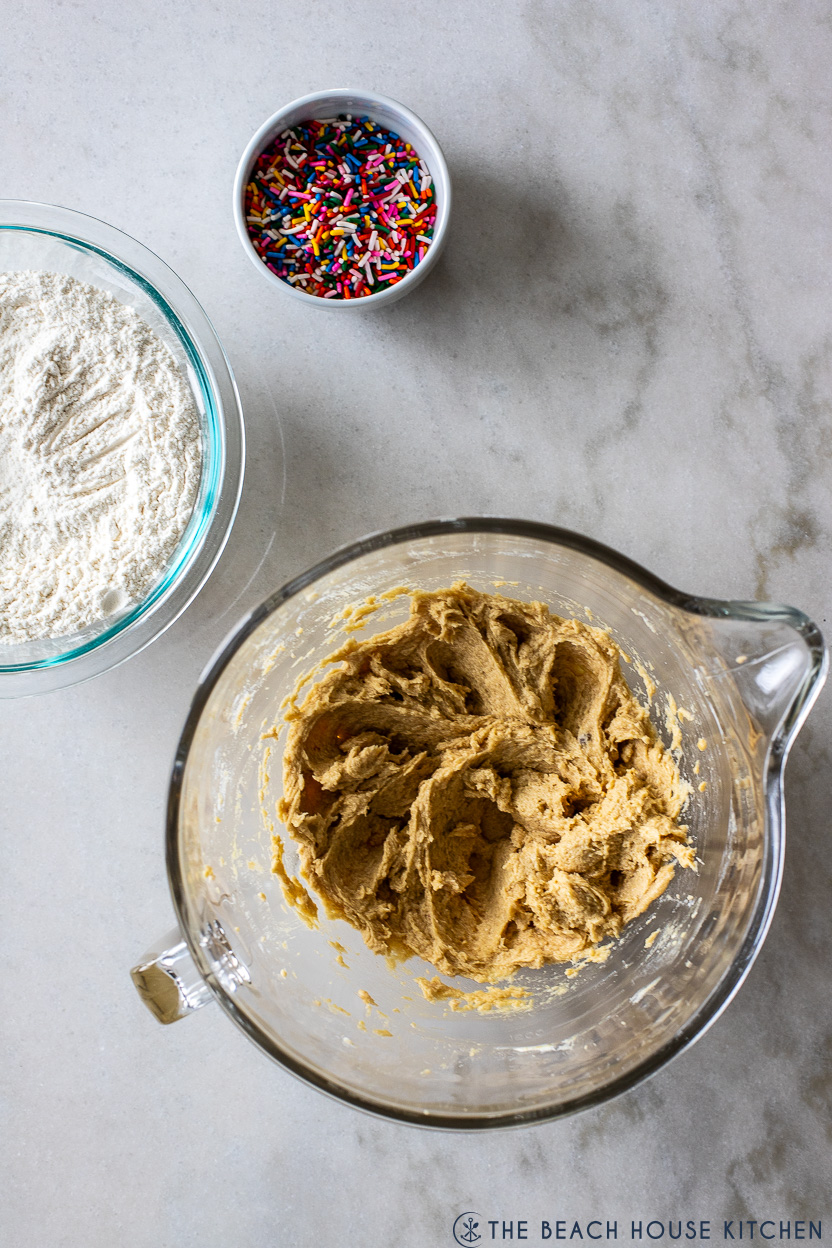 Overhead photo of a bowl of cookie dough with a bowl of flour and a bowl of sprinkles