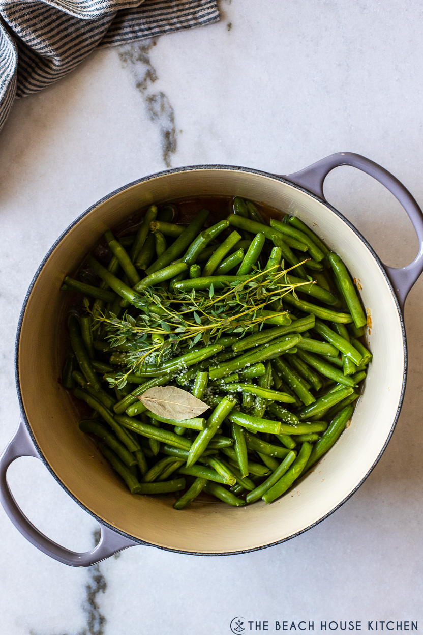 Overhead photo of a pot of green beans, thyme sprigs and a bay leaf