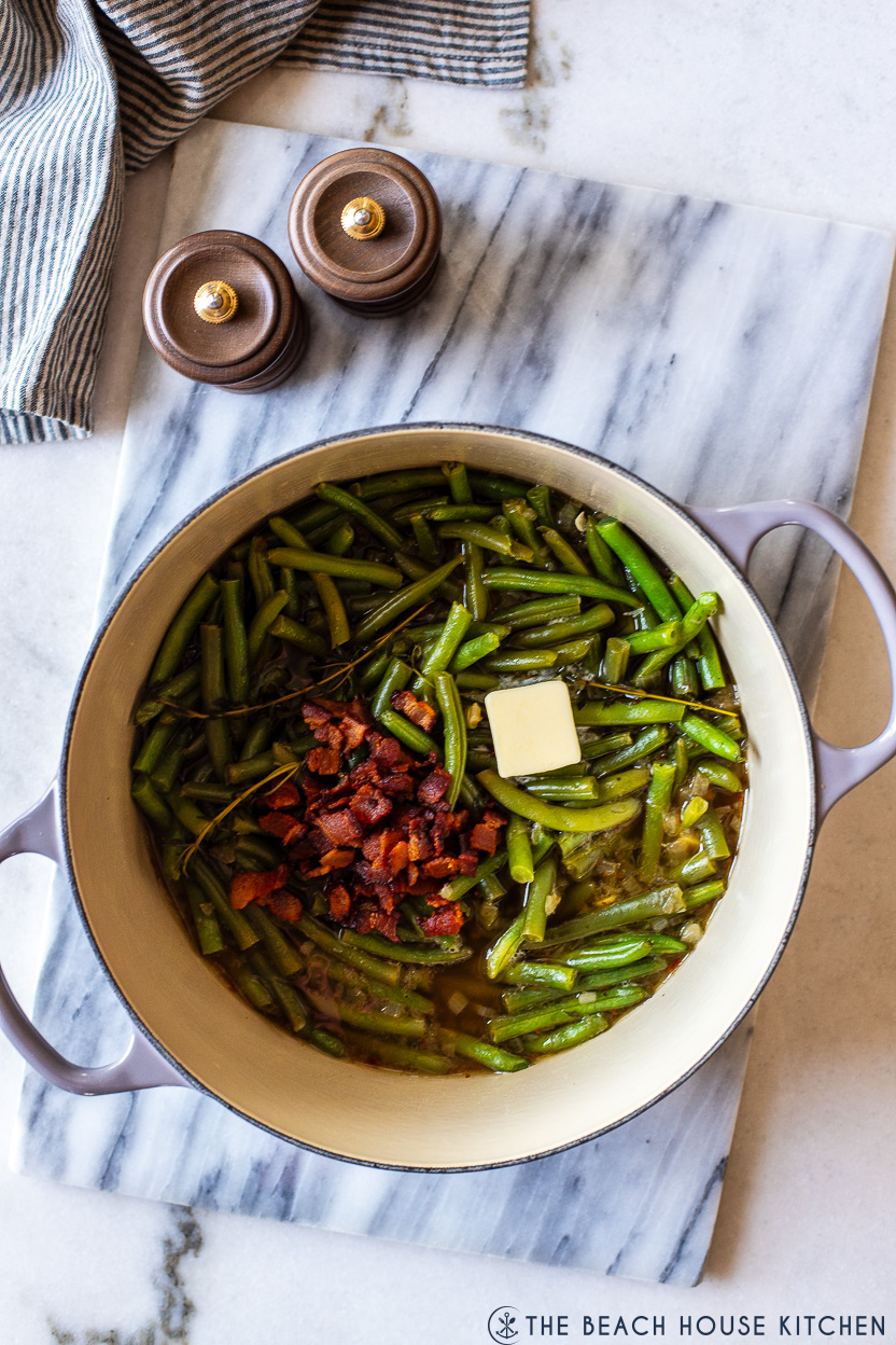 Overhead photo of a pot of green beans topped with chopped bacon and a pat of butter