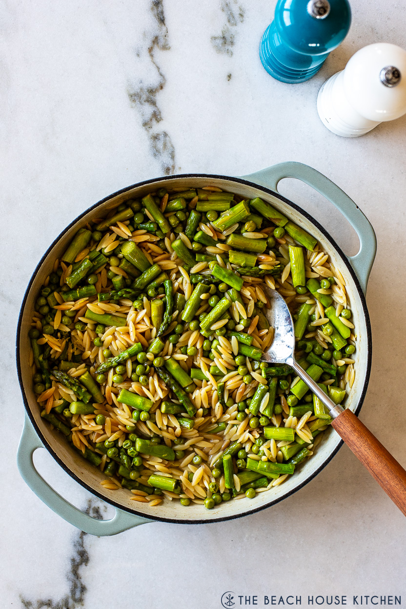 Overhead photo of a skillet of asparagus and pea orzo with salt and pepper shakers off to the side