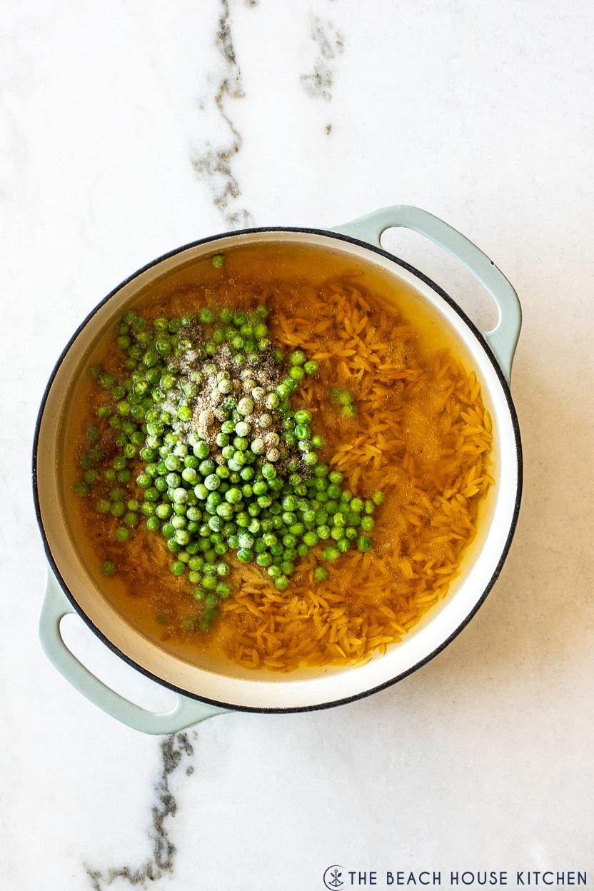 Overhead photo of a skillet filled with orzo, chicken broth and frozen peas