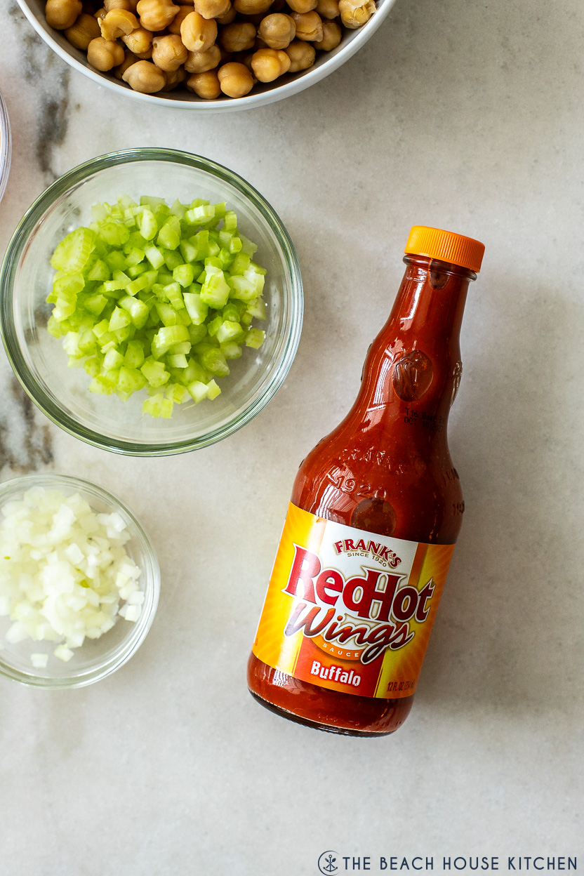 Up close overhead photo of a bottle of Frank's Buffalo wing sauce, a small bowl of chopped onions and a small bowl of chopped celery