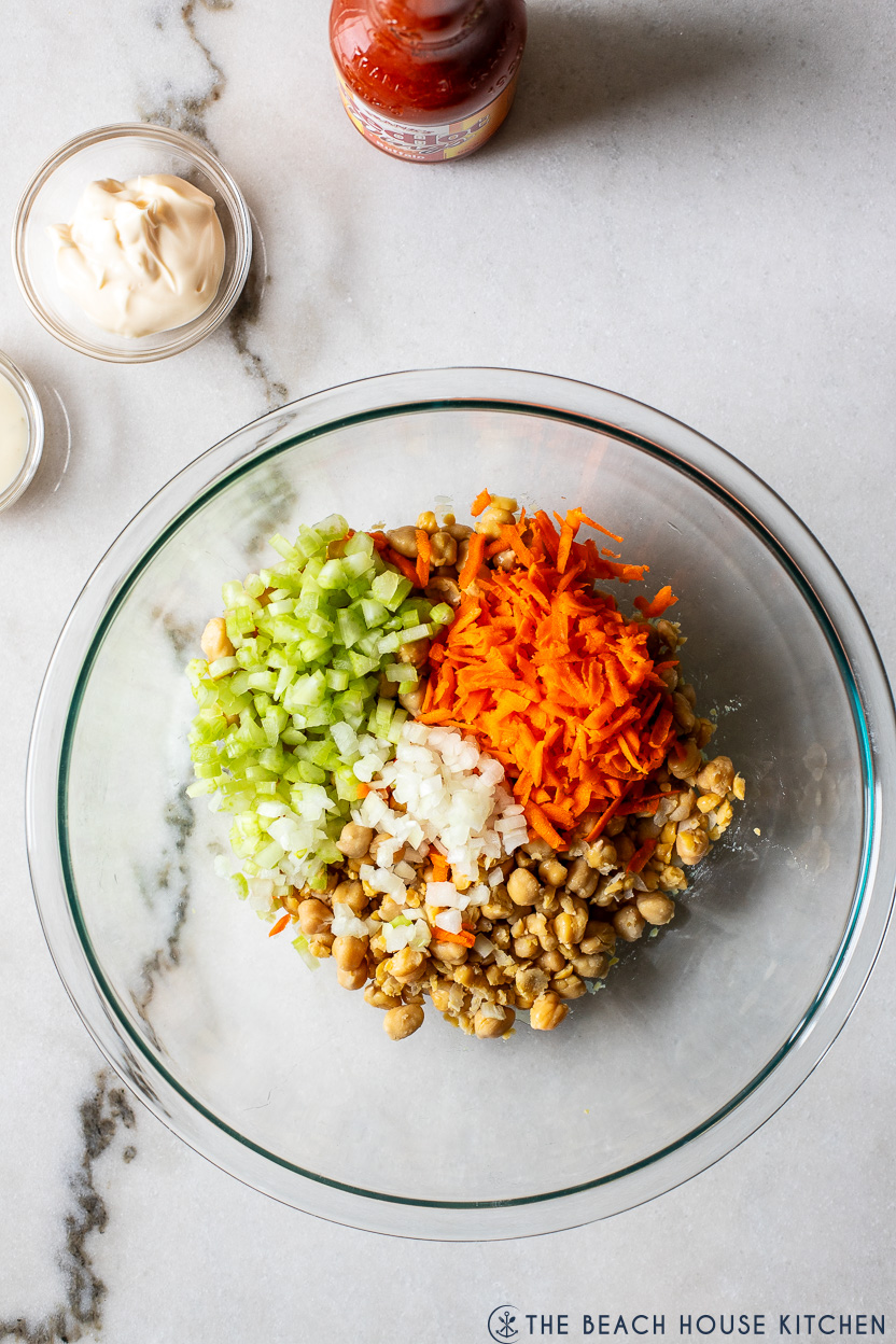 Overhead photo of a glass bowl of chickpeas, shredded carrots, chopped celery and chopped onion
