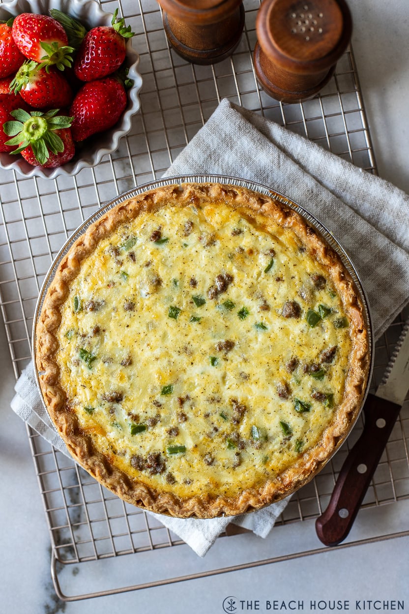 Up close overhead photo of a sausage pepper and onion quiche on a wire rack with a small bowl of straberries