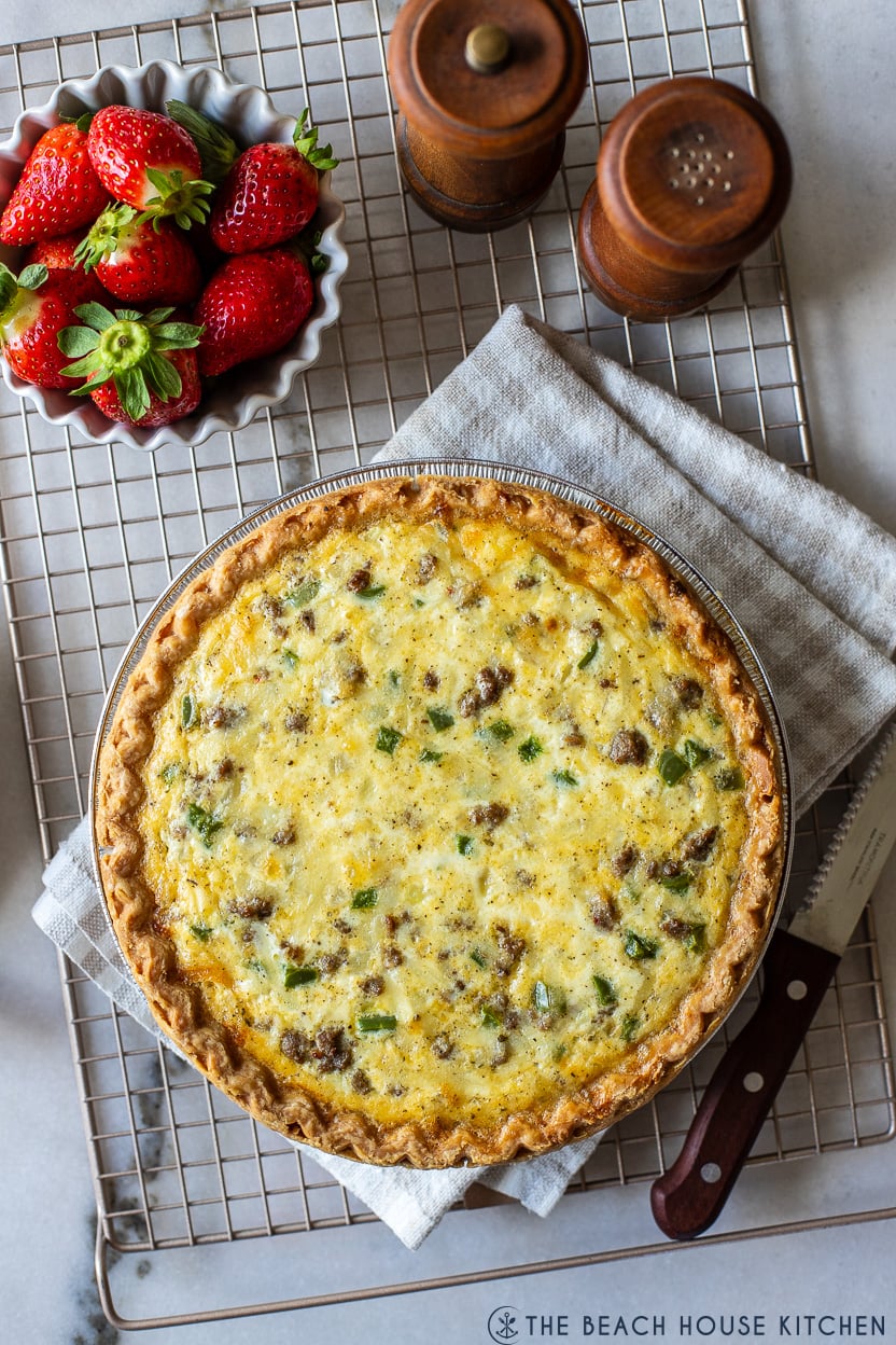 Overhead photo of a sausage pepper and onion quiche on a wire rack with a bowl of straberries and wooden salt and pepper shakers