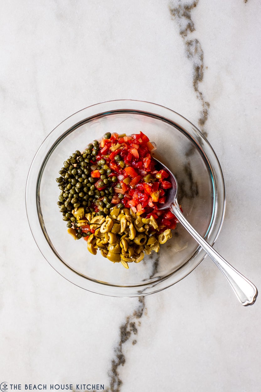 Overhead photo of a glass bowl filled with pico de gallo, green olives and capers