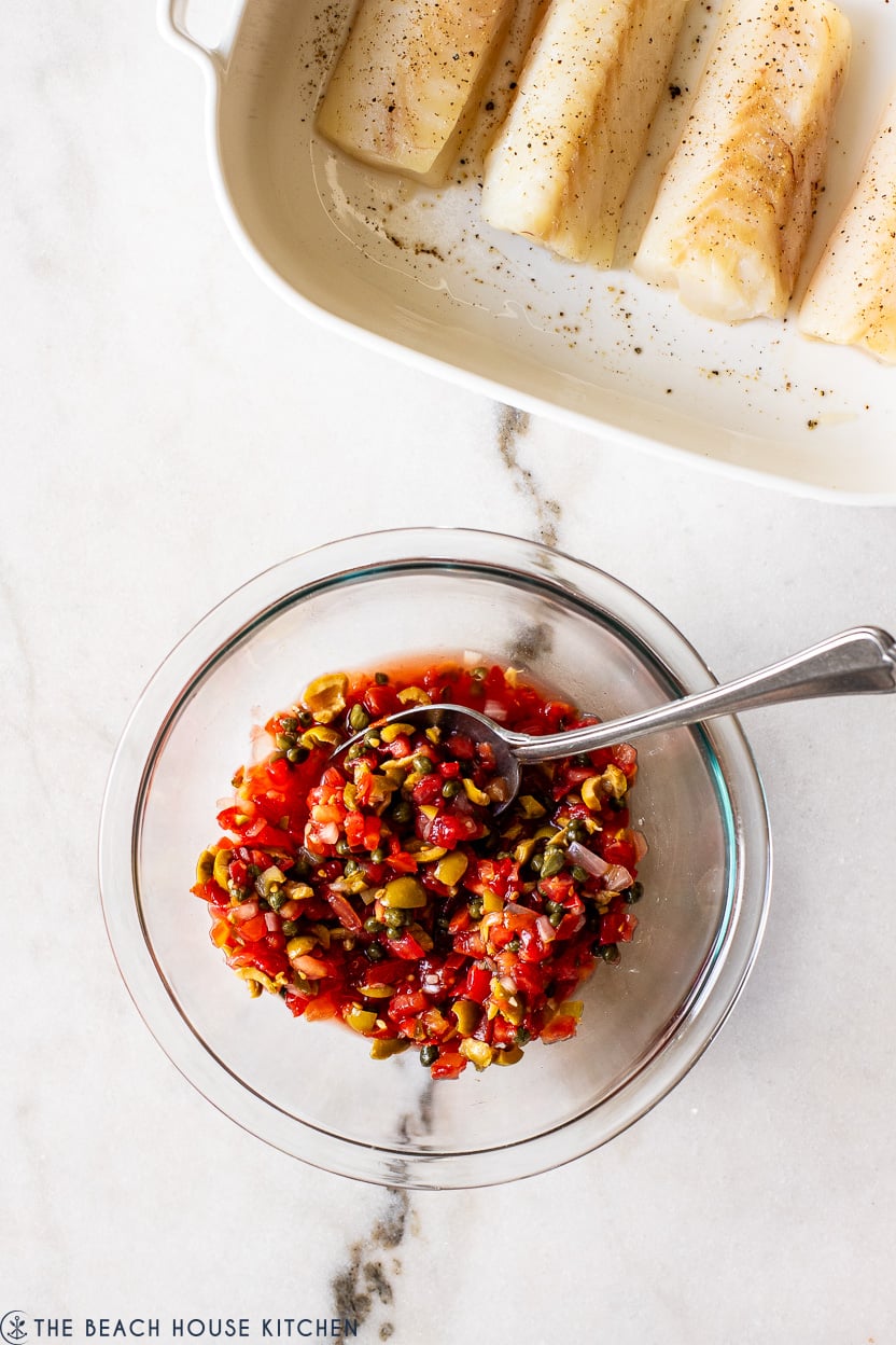 Overhead photo of a pico de gallo mixture in a glass bowl with a white baking dish with cod fillets off to the top right