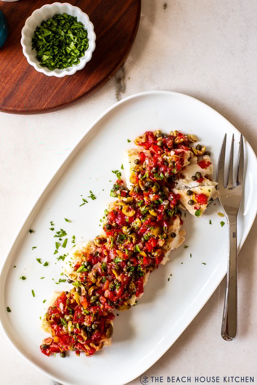 Up close overhead photo of a platter of baked cod with pico de gallo and olives