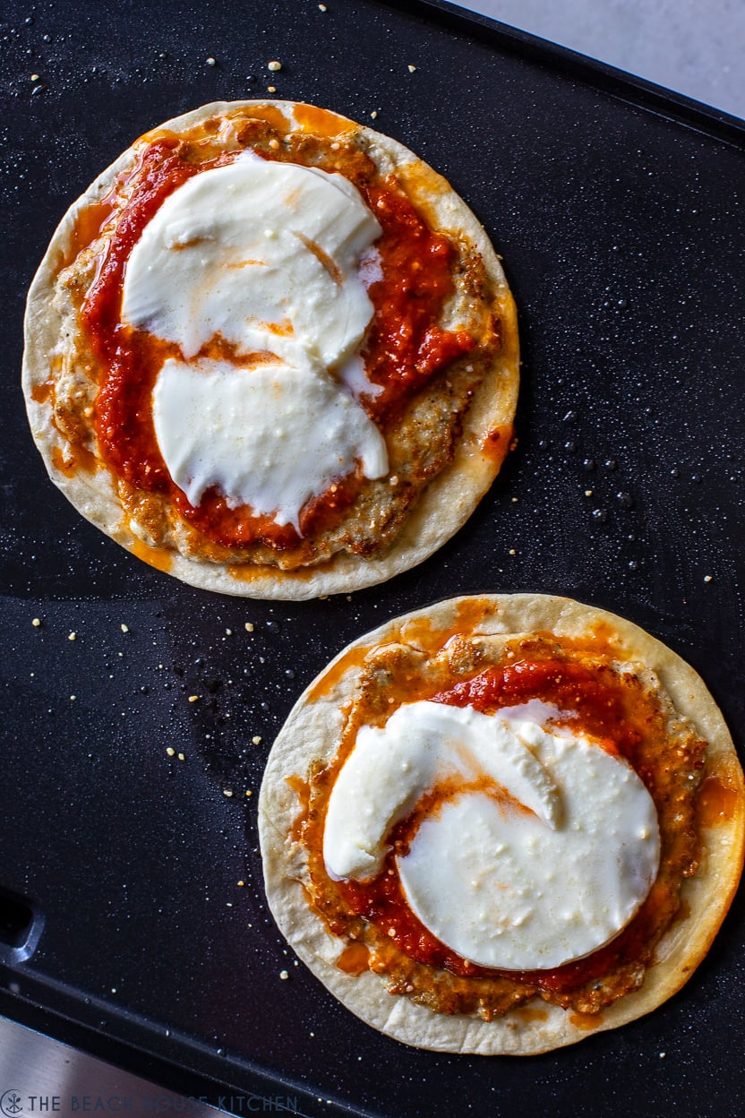 Overhead photo of two chicken parmesan smash tacos on a griddle