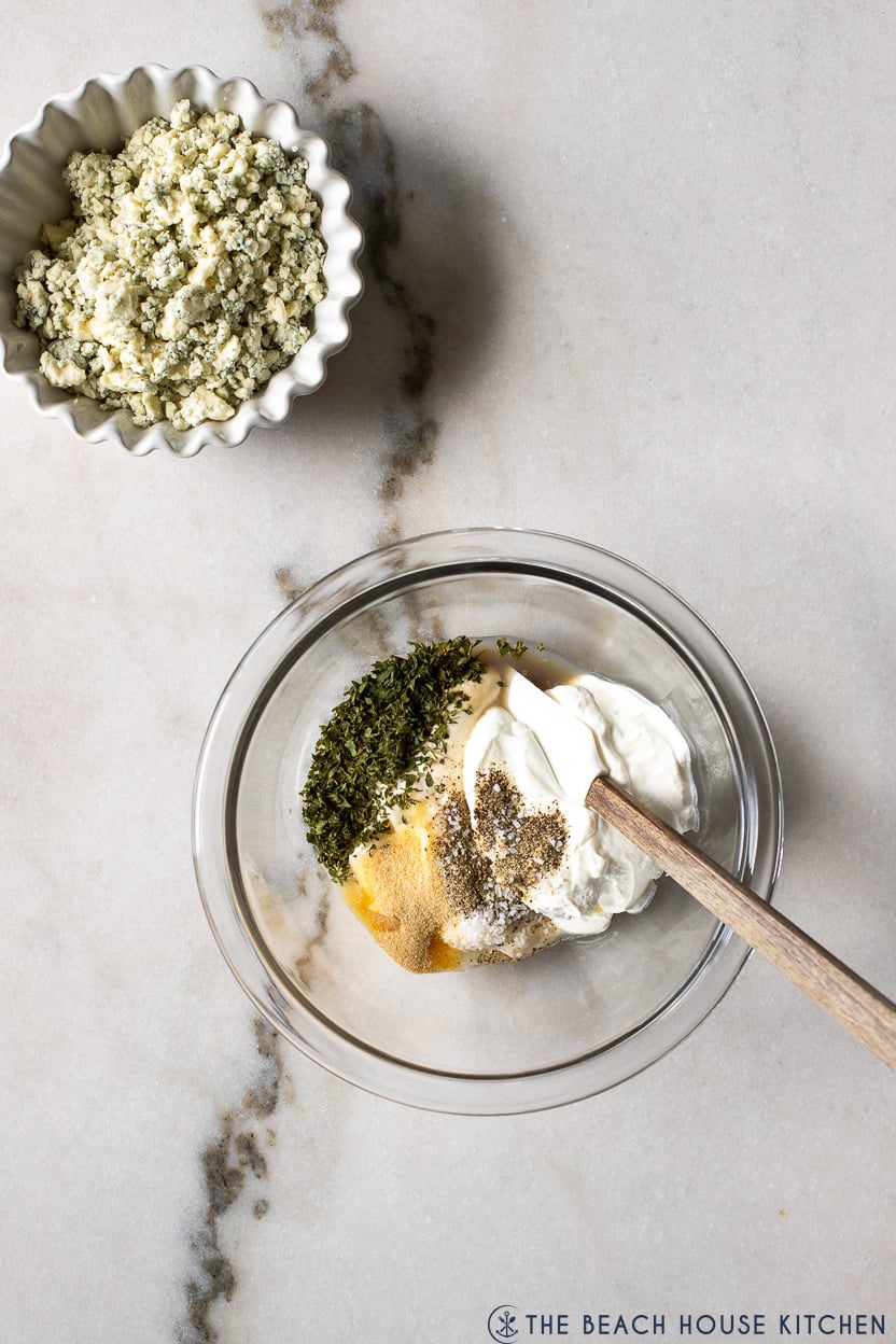 Overhead photo of a bowl of ingredients for a blue cheese dressing with a small bowl of blue cheese crumbls