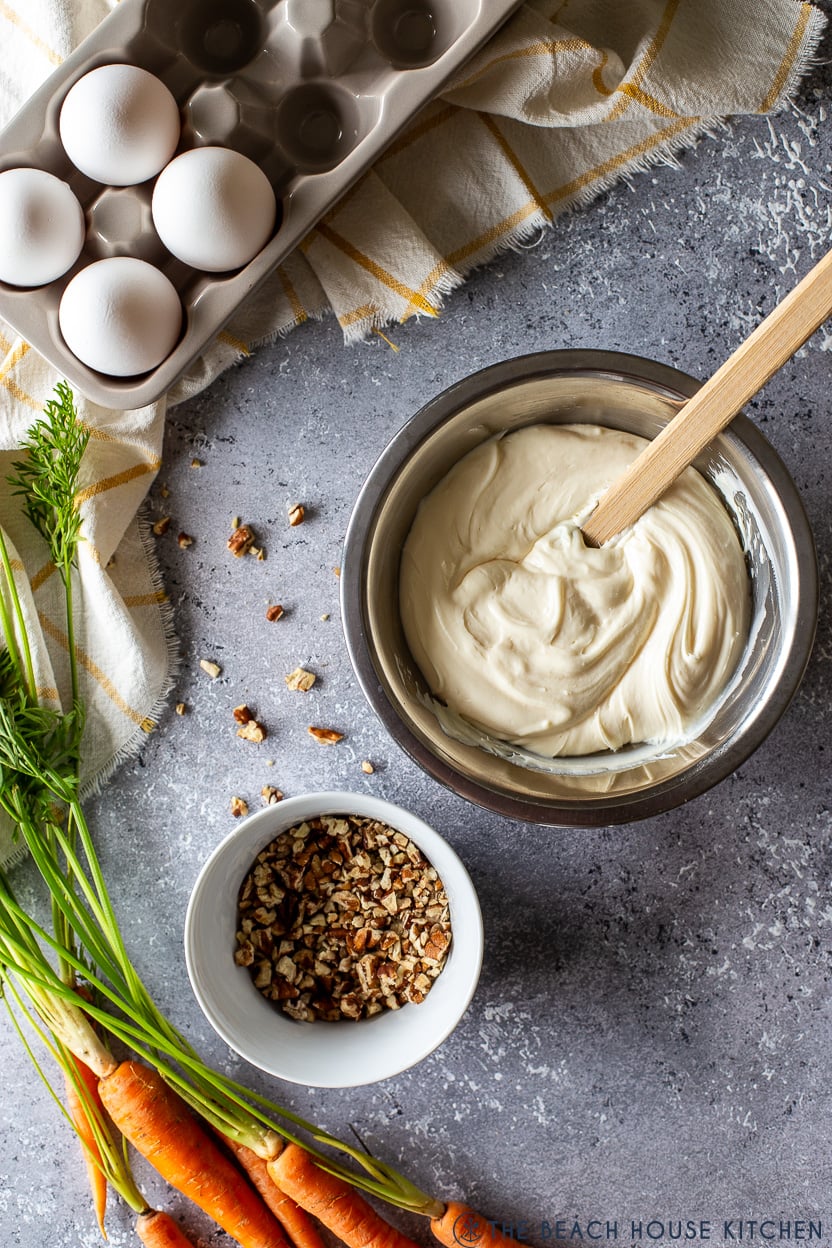 Overhead photo of a bowl of cream cheese frosting and a small bowl of pecans