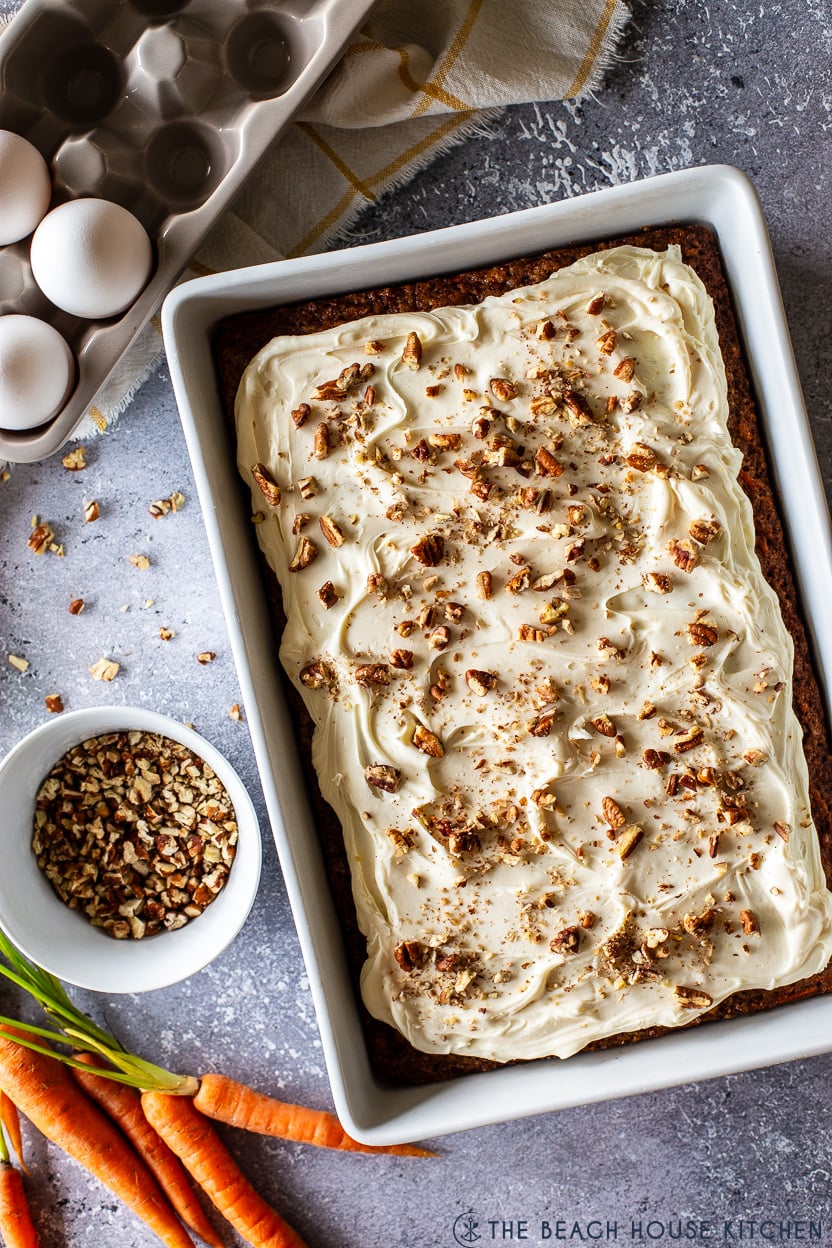 Overhead photo of a carrot cake with cream cheese frosting topped with chopped pecans