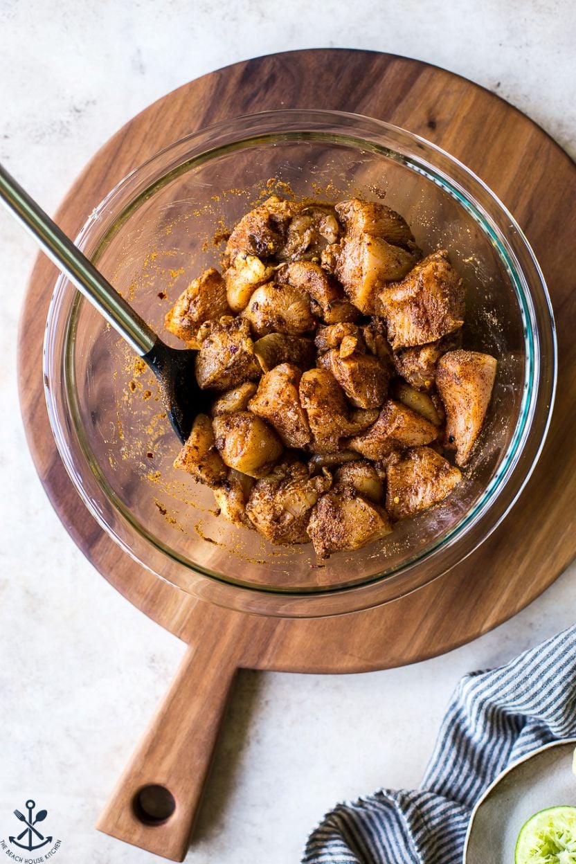 Overhead photo of a glass bowl filled with seasoned raw chicken pieces