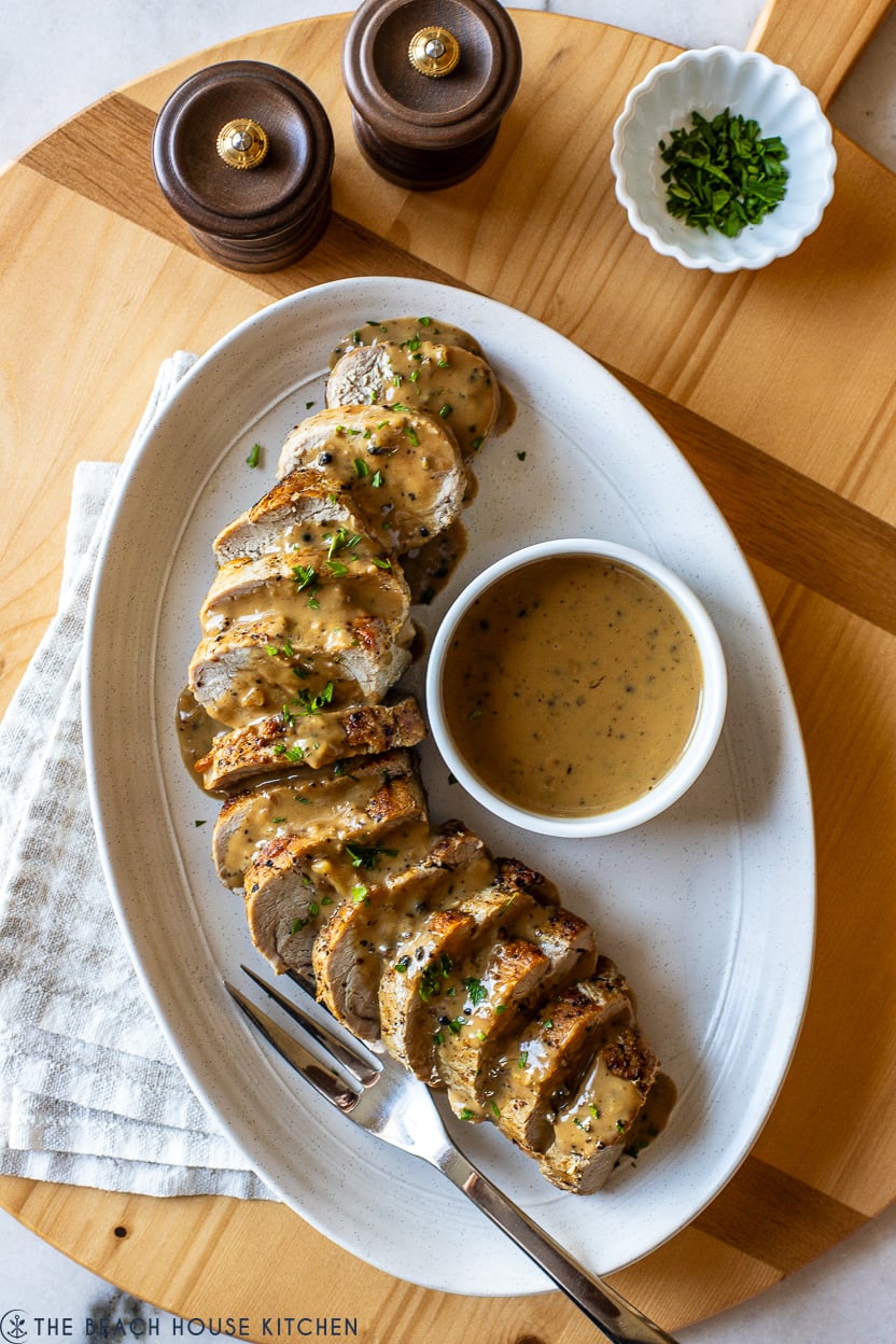 Overhead photo of an oval platter with a pork tenderloin topped with peppercorn sauce