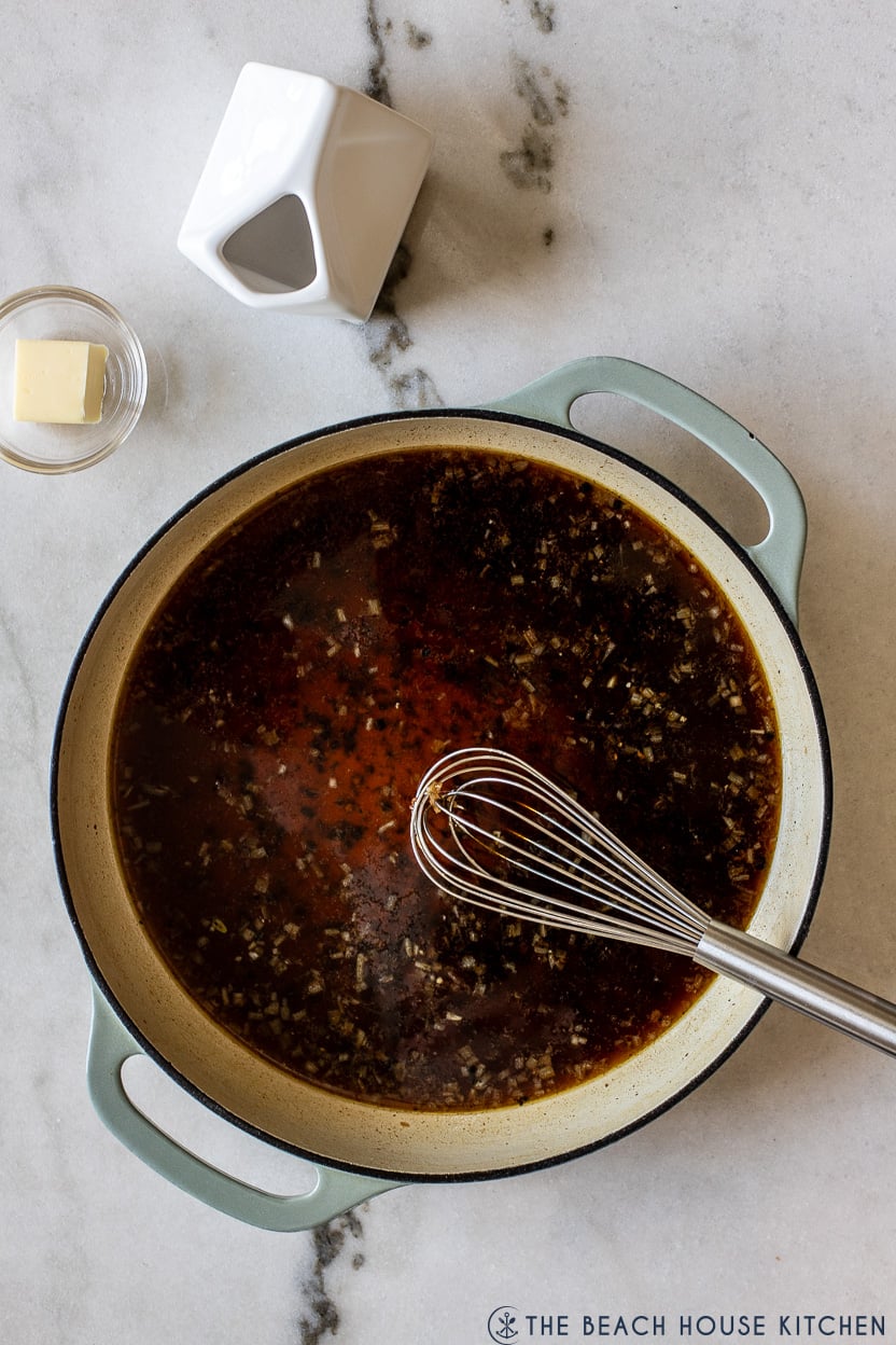 Overhead photo of skillet with beef broth and a whisk