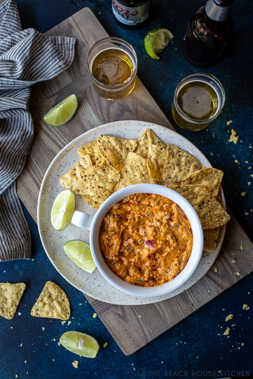 Overhead photo of a bowl of cheesy dip with chorizo on a plate with tortilla chips with two glasses of beer off to the side