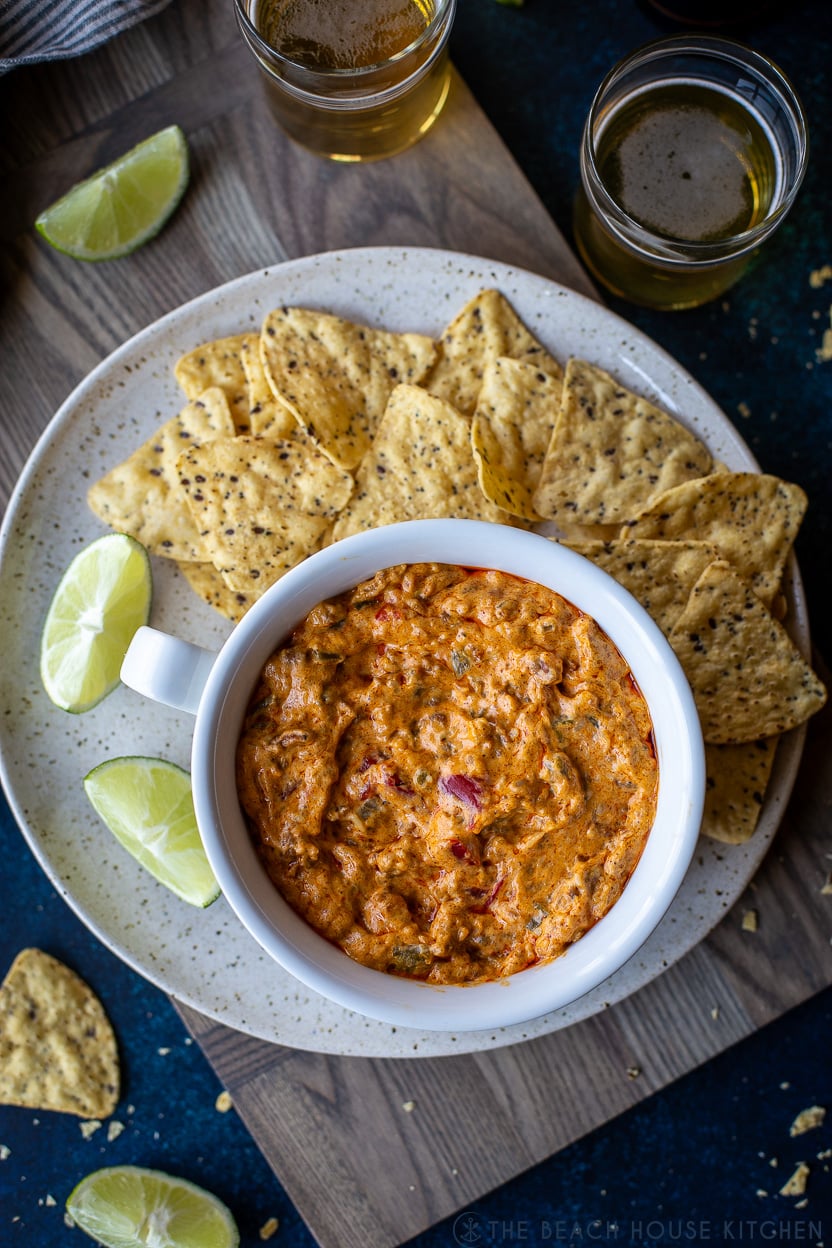 Up close Overhead photo of a white bowl of cheesy Mexican chorizo dip on a plate with tortilla chips and lime wedges