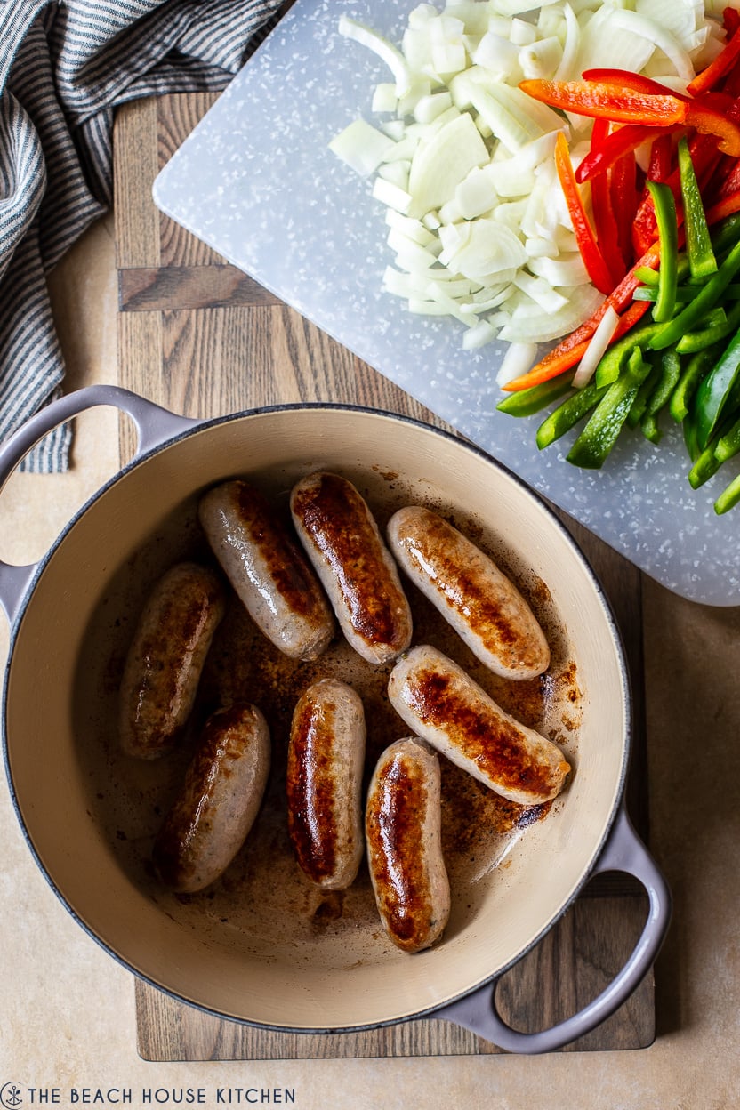 Overhead photo of a pot of browned sausages, and cut peppers and onions