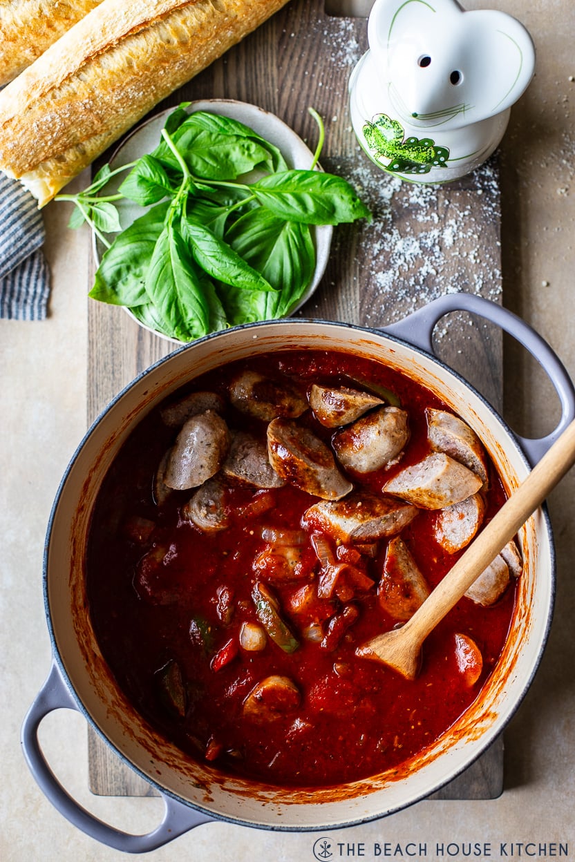 Overhead photo of a pot of sliced Italian sausage pieces on top of some sauce, peppers and onions