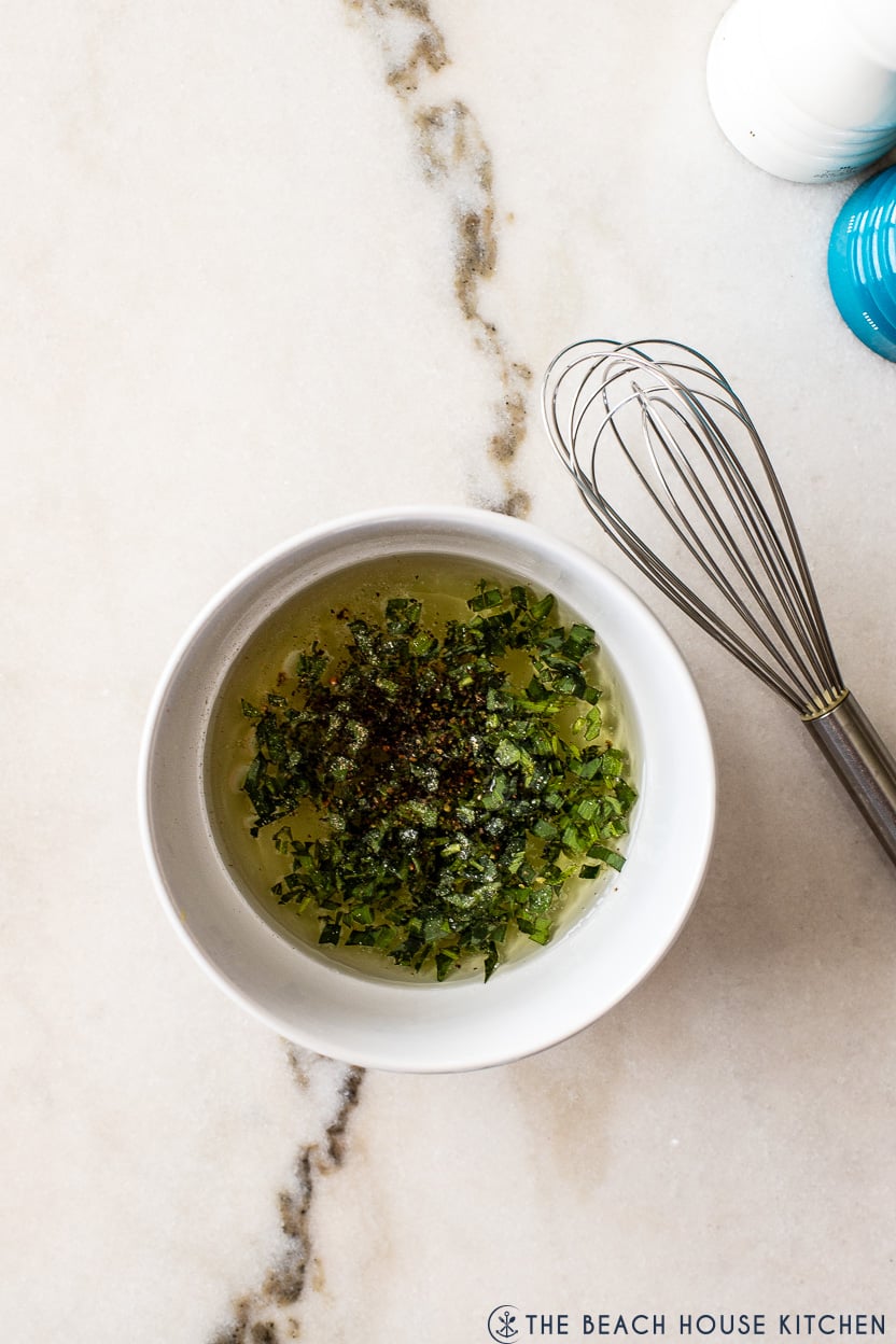 Overhead photo of tarragon vinagrette in a small white bowl with a silver whisk off to the side