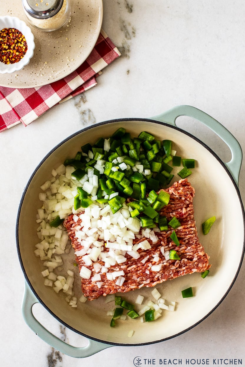 Overhead photo of a deep skillet filled with onions, green peppers and bulk Italian sausage meat