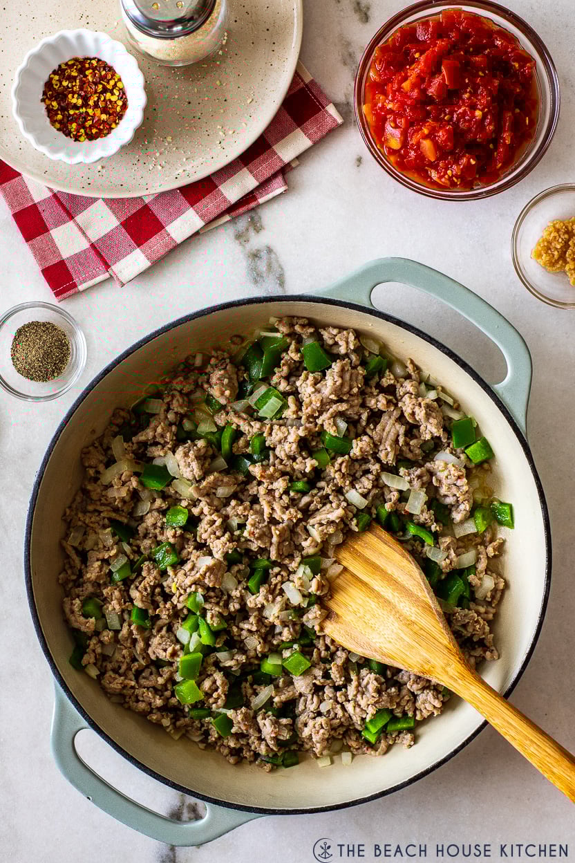 Overhead photo of a deep skillet filled wit cooked Italians sausage crumbles and onions and peppers