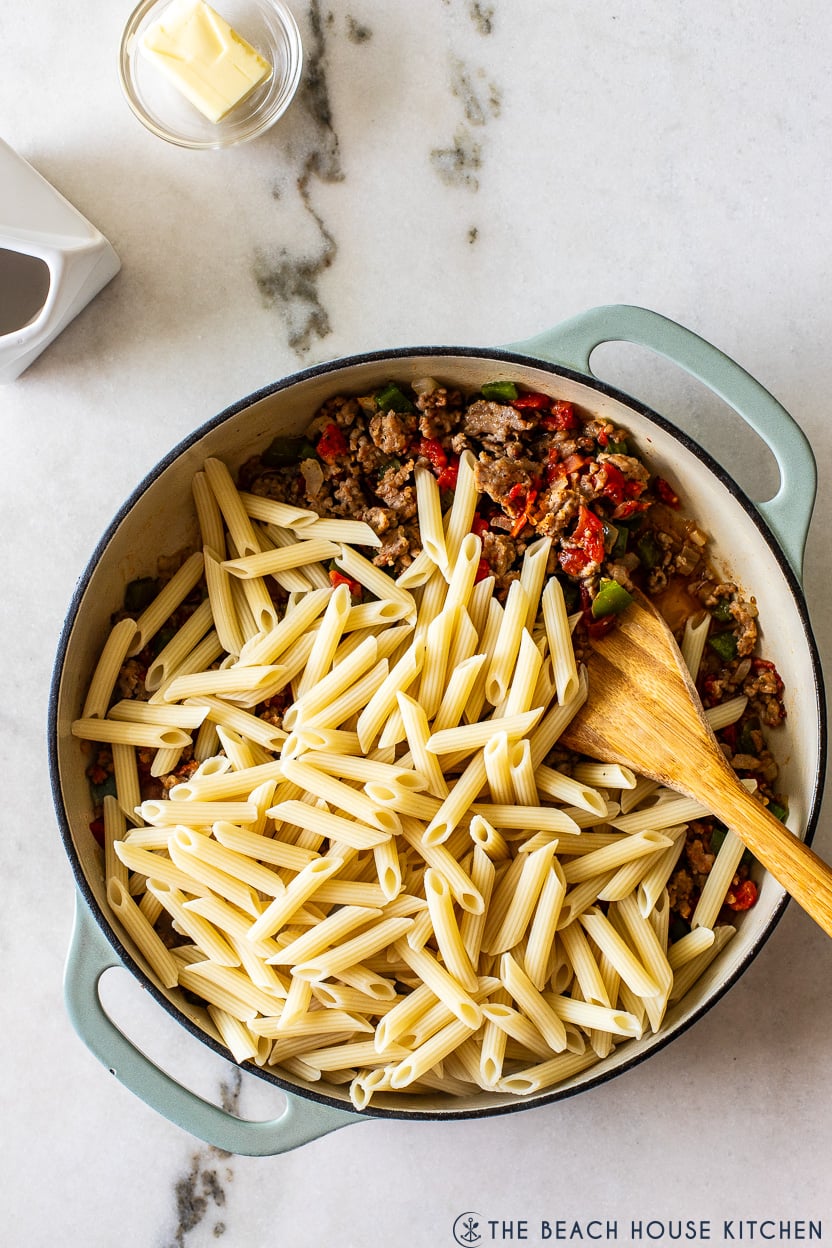Overhead photo of a skillet filled with a sausage mixture topped with cooked penne pasta