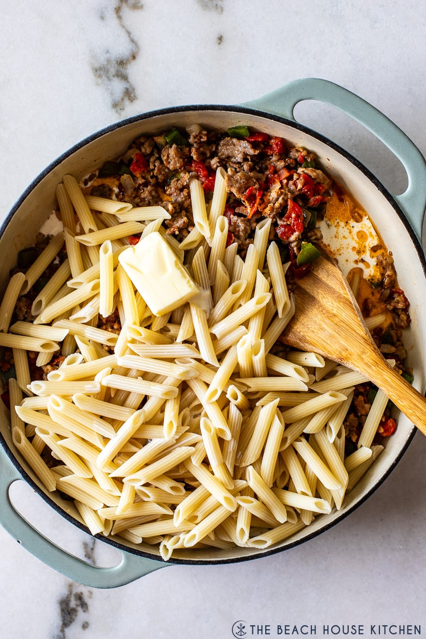 Overhead photo of a skillet filled with an Italian sausage mixture, cooked penne pasta and butter
