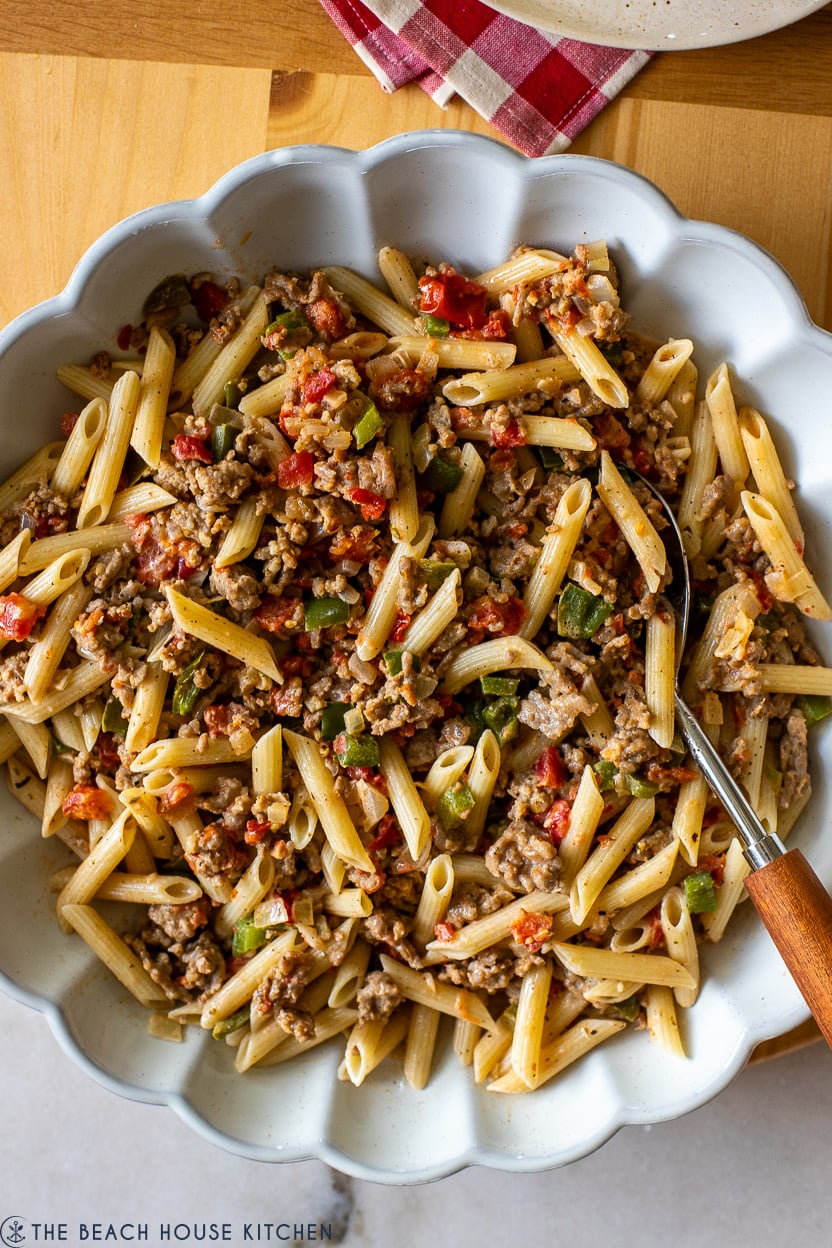 Up close overhead photo of a white scallopped dish filled with Penne with Italian Sausage Tomatoes Peppers and Onions