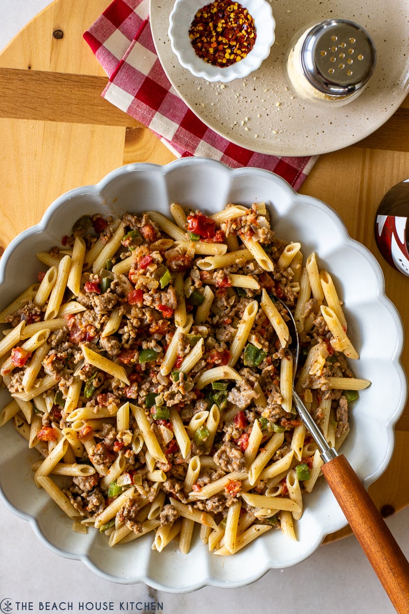 Overhead photo of a white scalloped dish filled with Penne with Italian Sausage Tomatoes Peppers and Onions