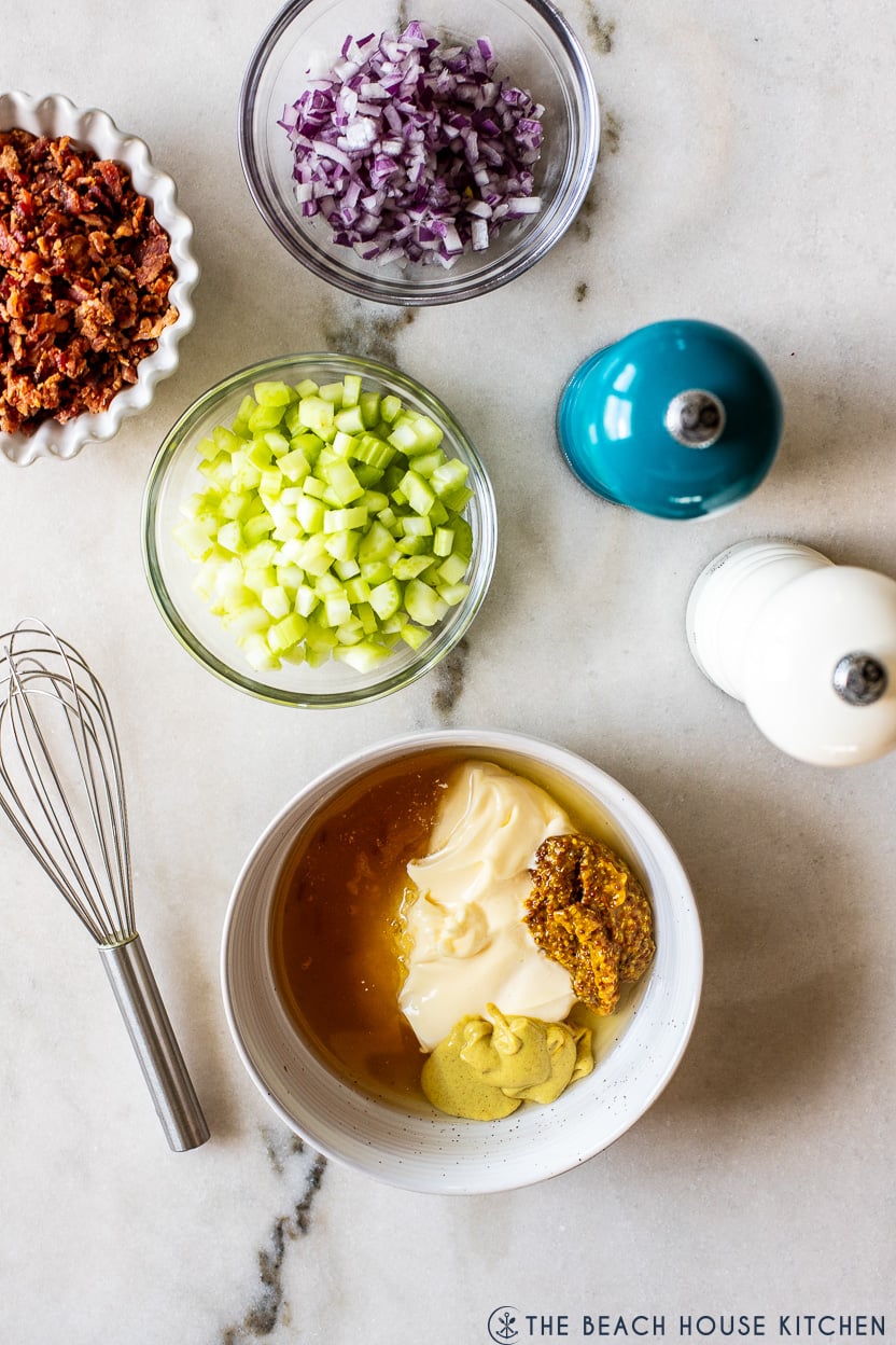 Overhead photo of a bowl of pre-mixed honey mustard dresing, a bowl of bacon bits, red onions and chopped celery.