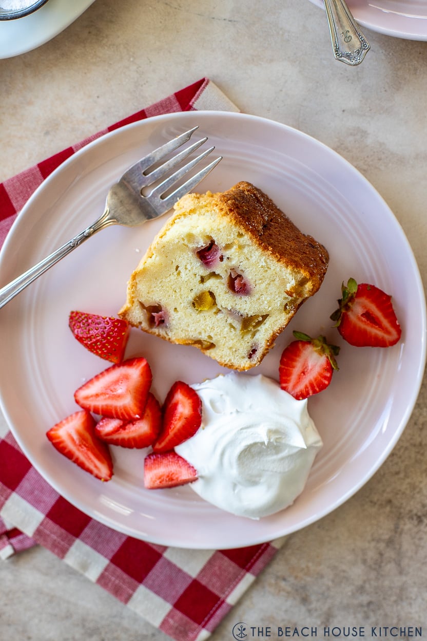 Up close overhead photo of a slice of strawberry mango pound cake on a pink plate with fresh strawberries and whipped cream