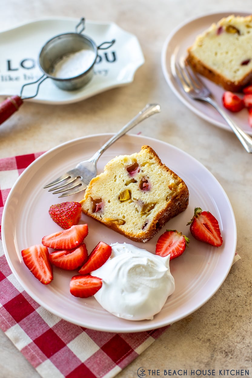 Up close photo of a slice of straberry mango pound cake on a pink plate with fresh strawberries and whipped cream