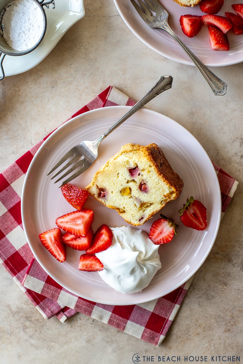 Overhead photo of a slice of strawberry mango pound cake on a pink plate with fresh cut strawberries and whipped cream