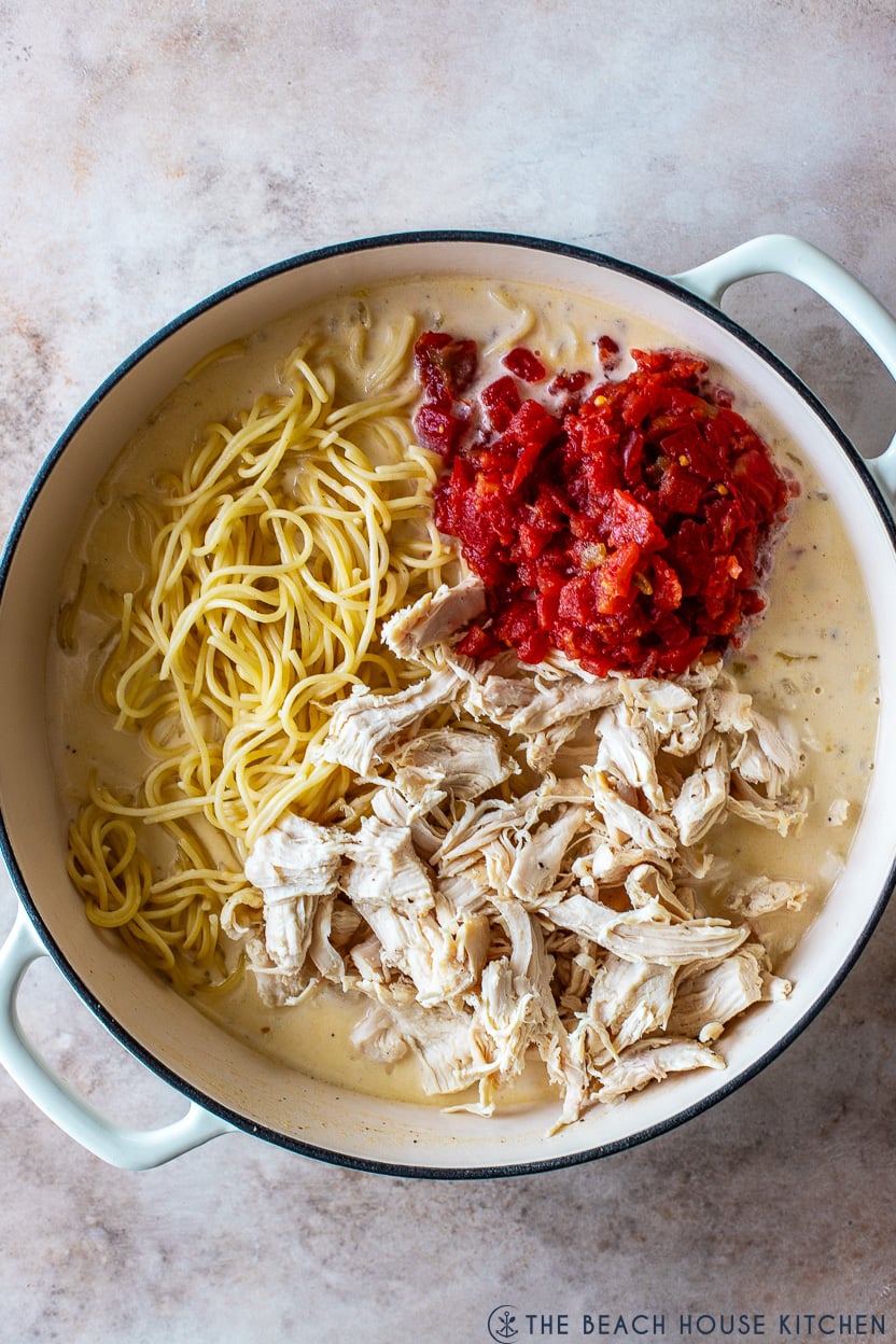 Overhead photo of a round skillet filled with a creamy sauce, tomatoes, shredded chicken and spaghetti