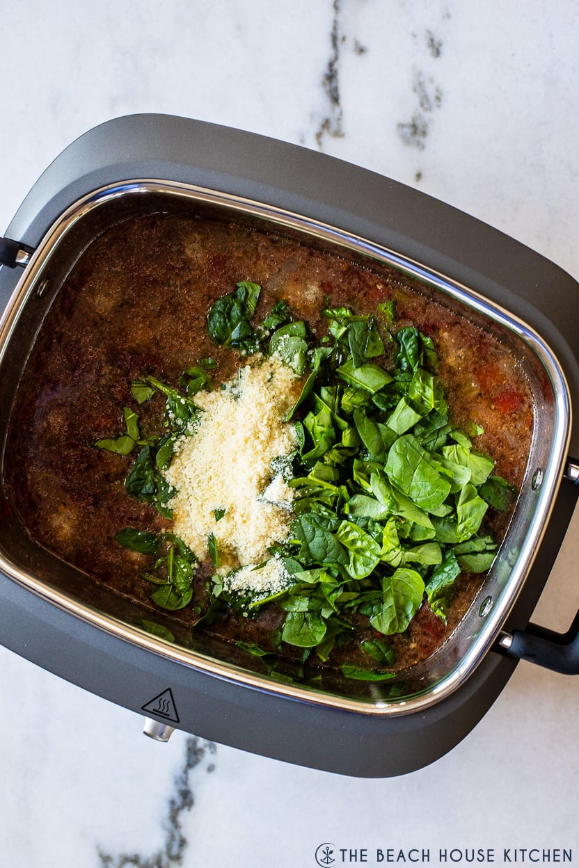 Overhead photo of a pot filled with Italian Meatball soup topped with spinach leaves and grated parmesan cheese