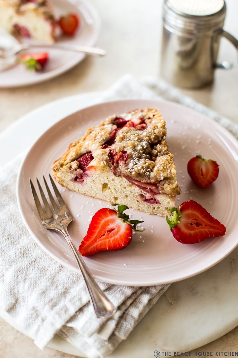 Up close photo of a slice of strawberry buckle on a pink plate with strawberry slices