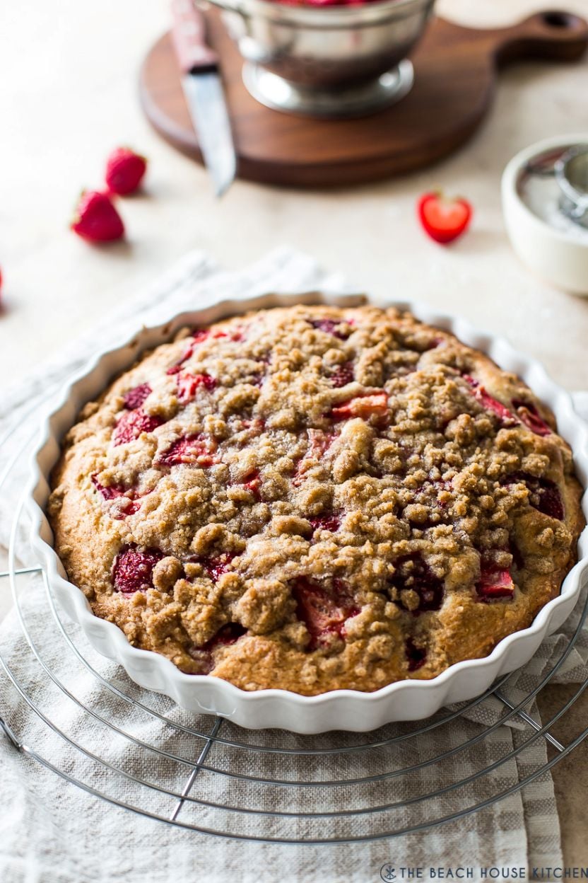 Up close photo of a strawberry buckle in a white scallopped baking dish on a round wire rack