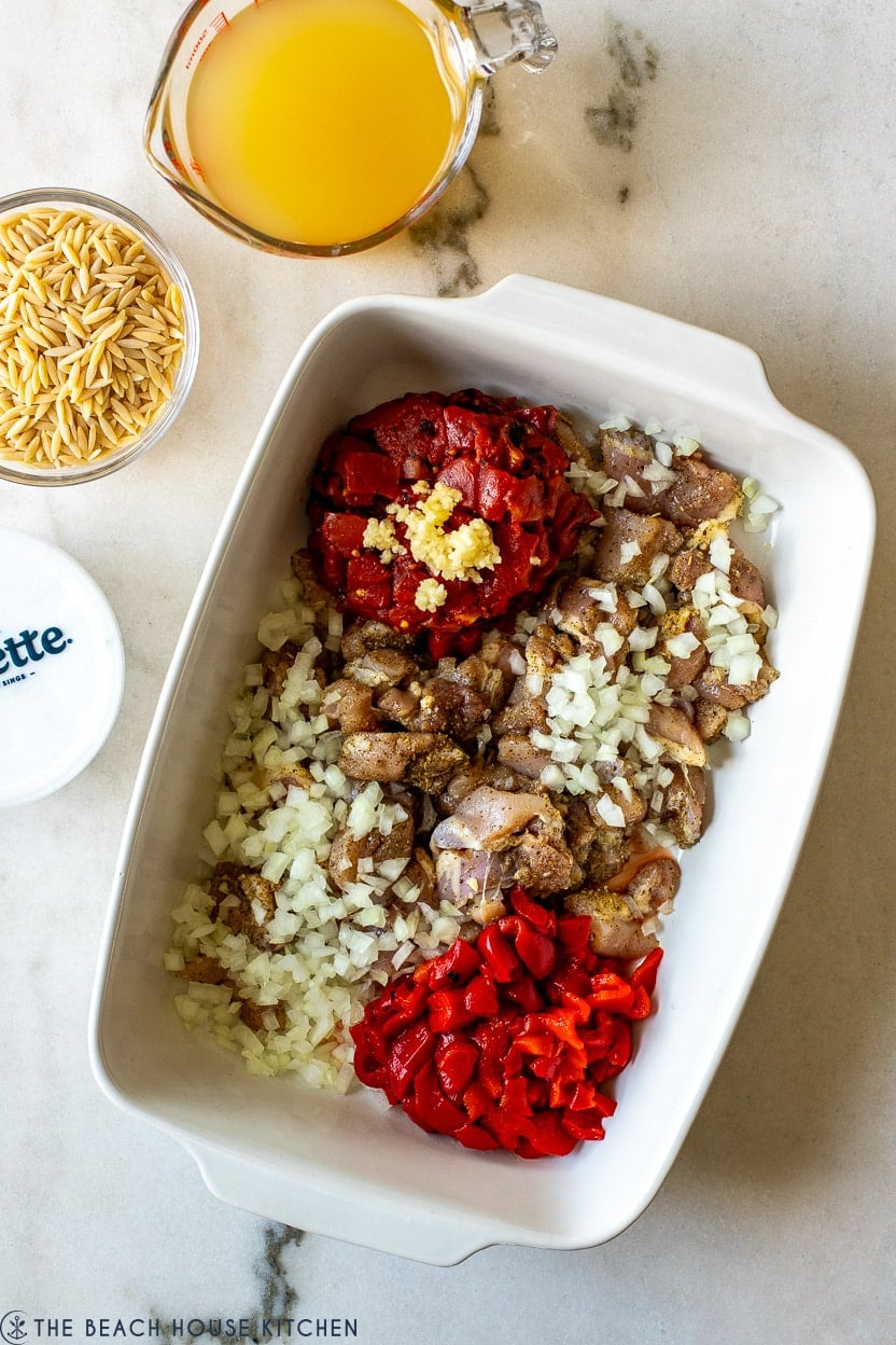 Overhead photo of 9x13 white dish filled with cubed chicken, tomatoes, onions and roasted red peppers