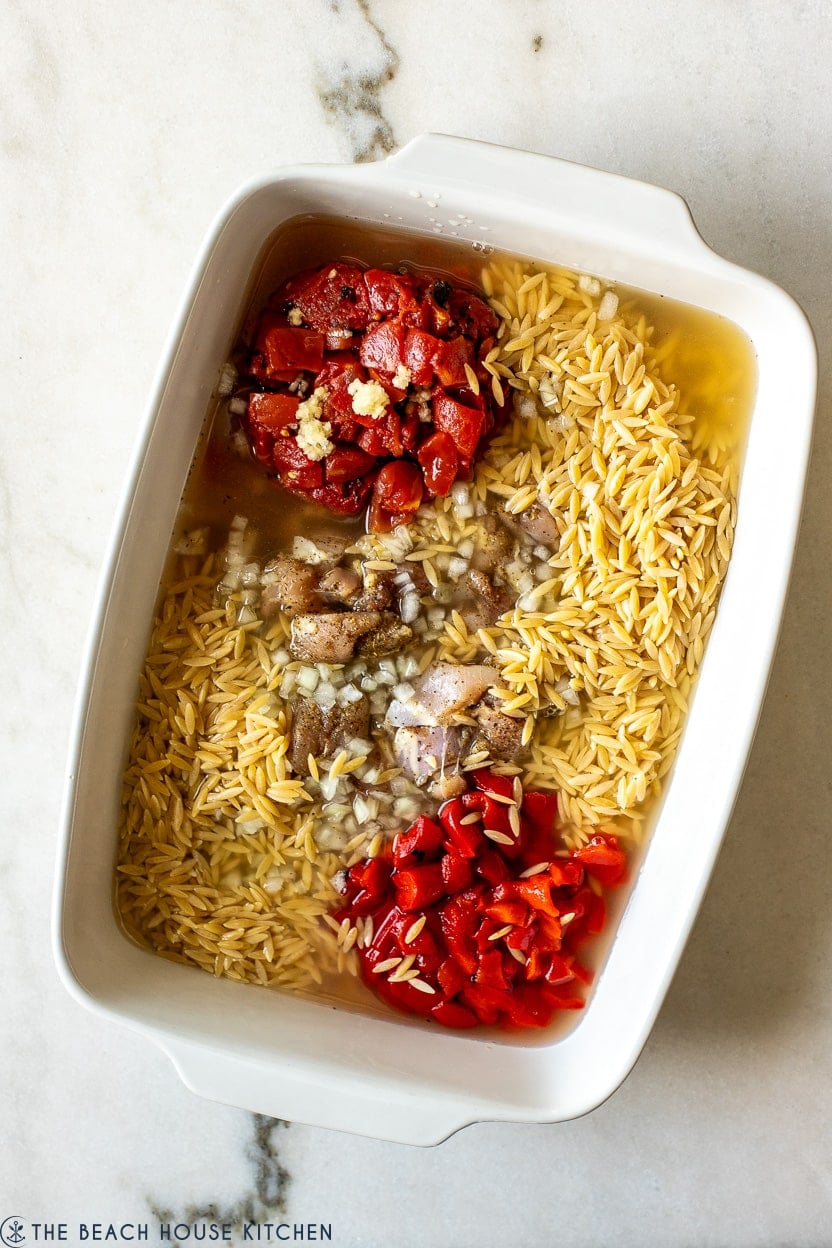 Overhead photo of a white 9x13 baking dish filled with pre-cooked chicken and veggies with orzo