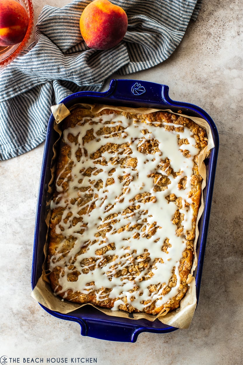 Overhead photo of glaze drizzled peach streusel bars in a blue baking dish