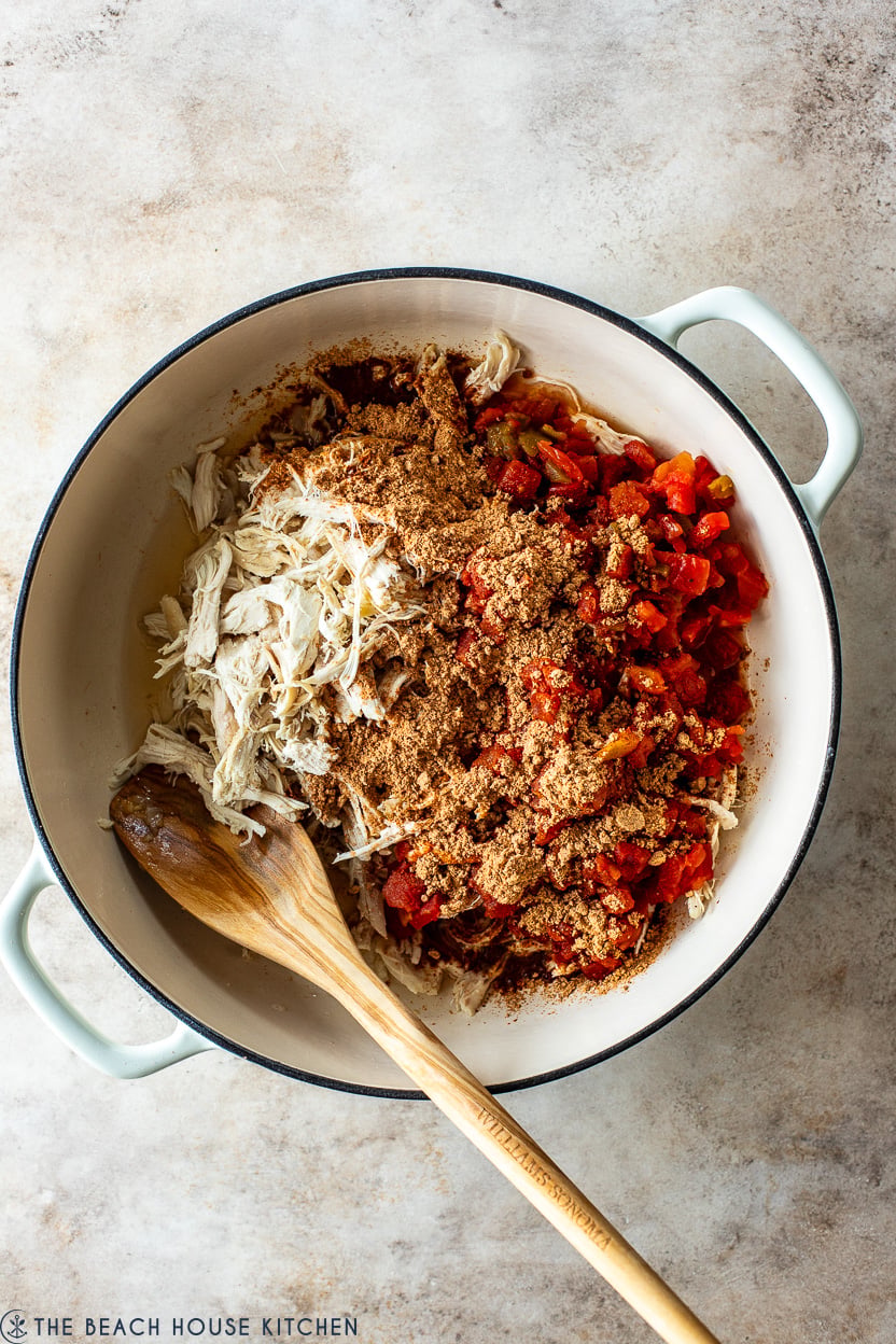 Overhead photo of a skillet filled with shredded chicken, tomatoes and taco seasoning