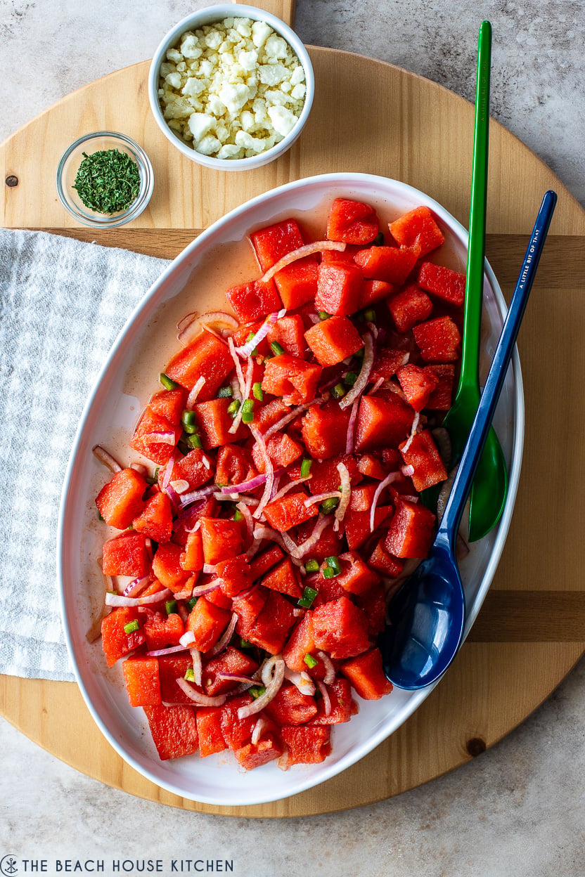 Overhead photo of a watermelon salad on a white platter on a round wooden board