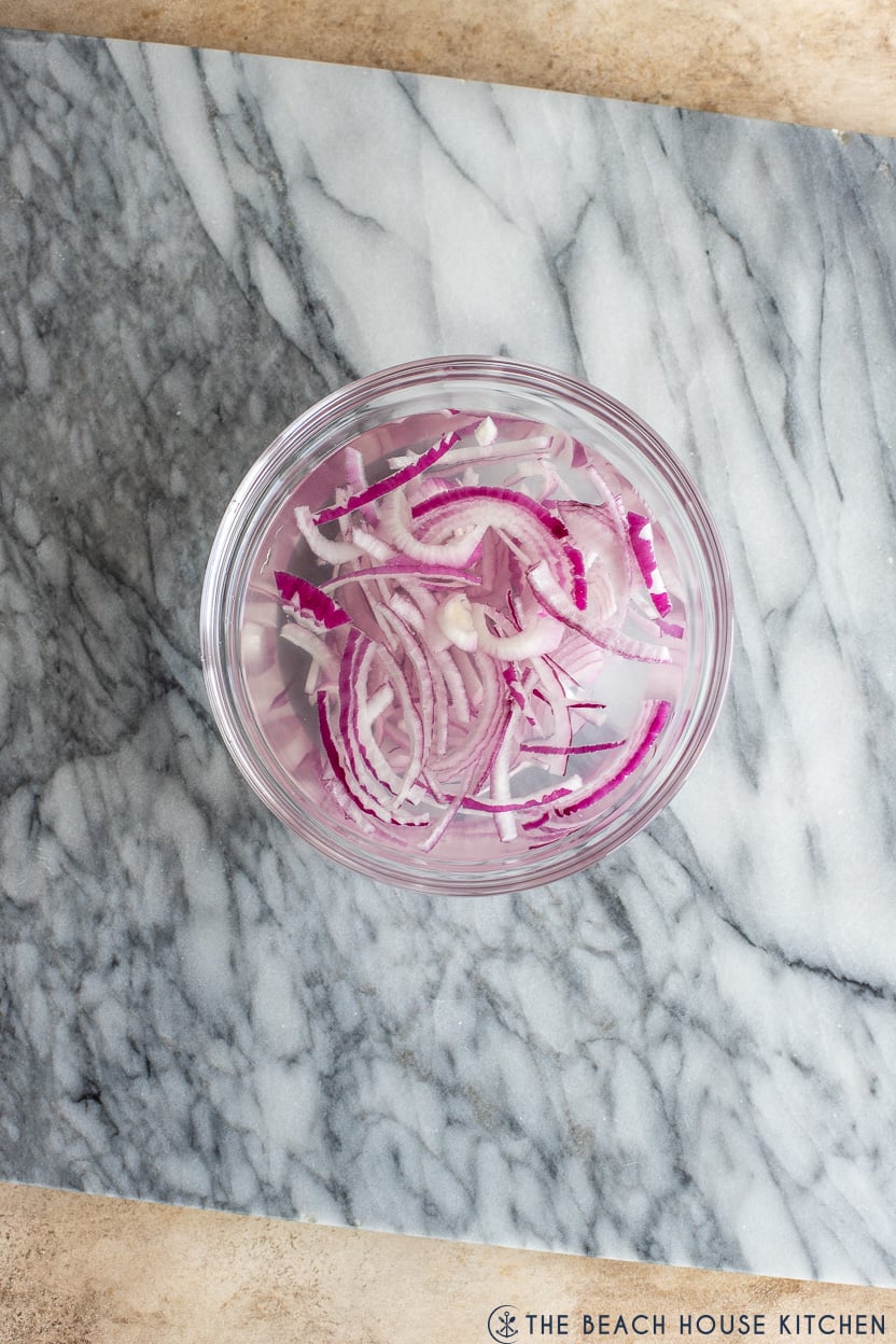 Overhead photo a a small glass bowl filled ith sliced red onion and water