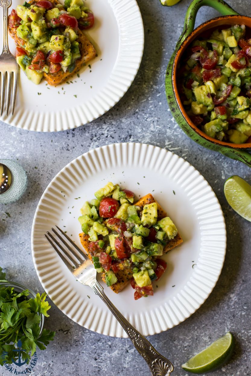 Overhead photo of salmon topped with avocado and tomato salsa on a white plate with a fork