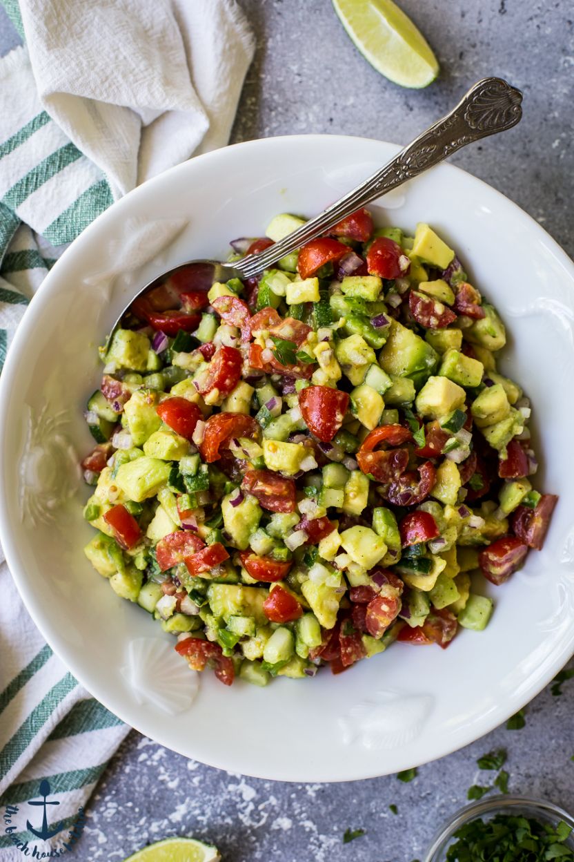 Up close overhead photo of avocado and tomato salsa in a white bowl with a spoon